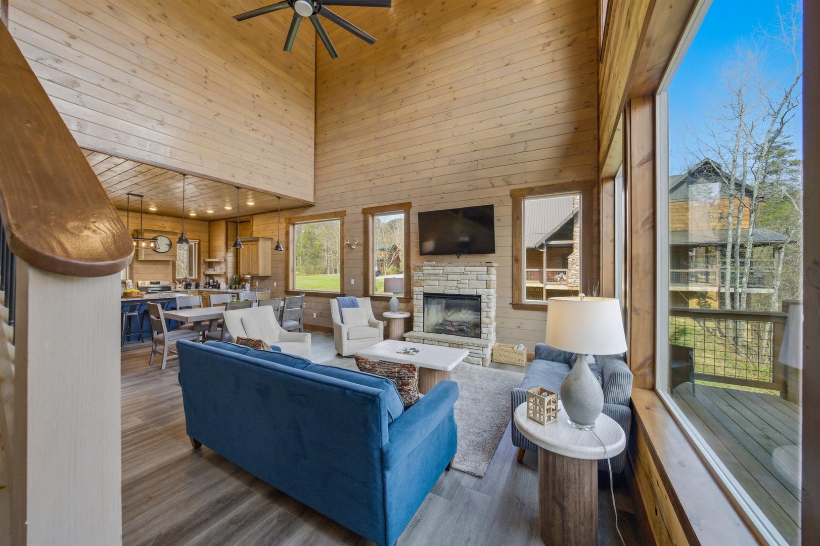 Relax in your open-concept living space featuring soaring wood ceilings, cozy fireplace, and floor-to-ceiling windows flooding the room with natural light.
