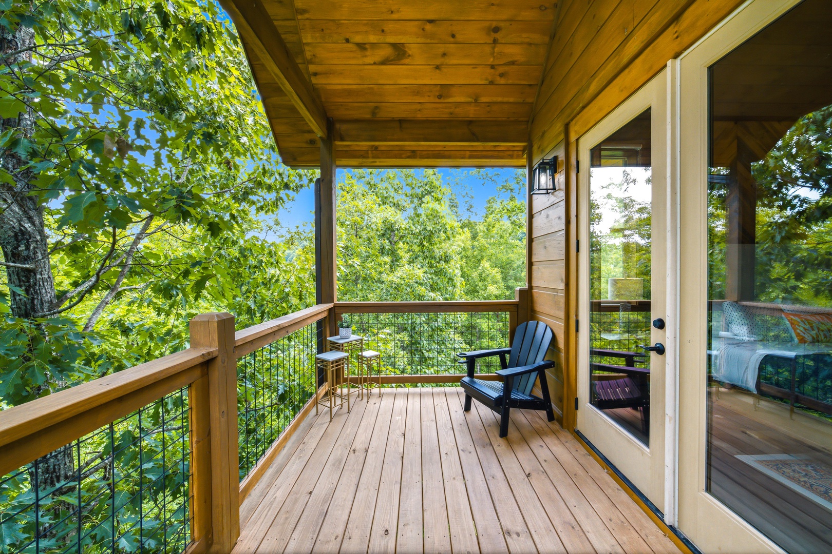 Peaceful covered deck framed by lush green trees, offering your own quiet spot to unwind with morning coffee or an evening read—your treetop sanctuary awaits.