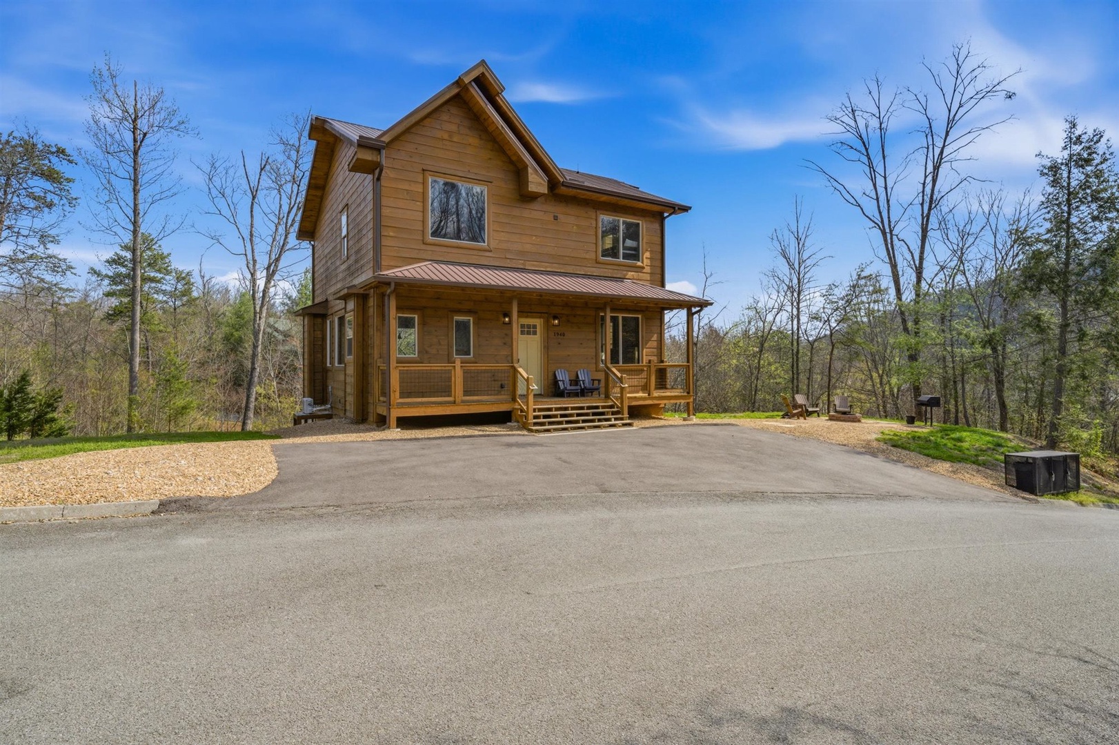 Beautiful two-story wooden cabin nestled among mature trees with convenient paved parking and spacious front porch for relaxing.