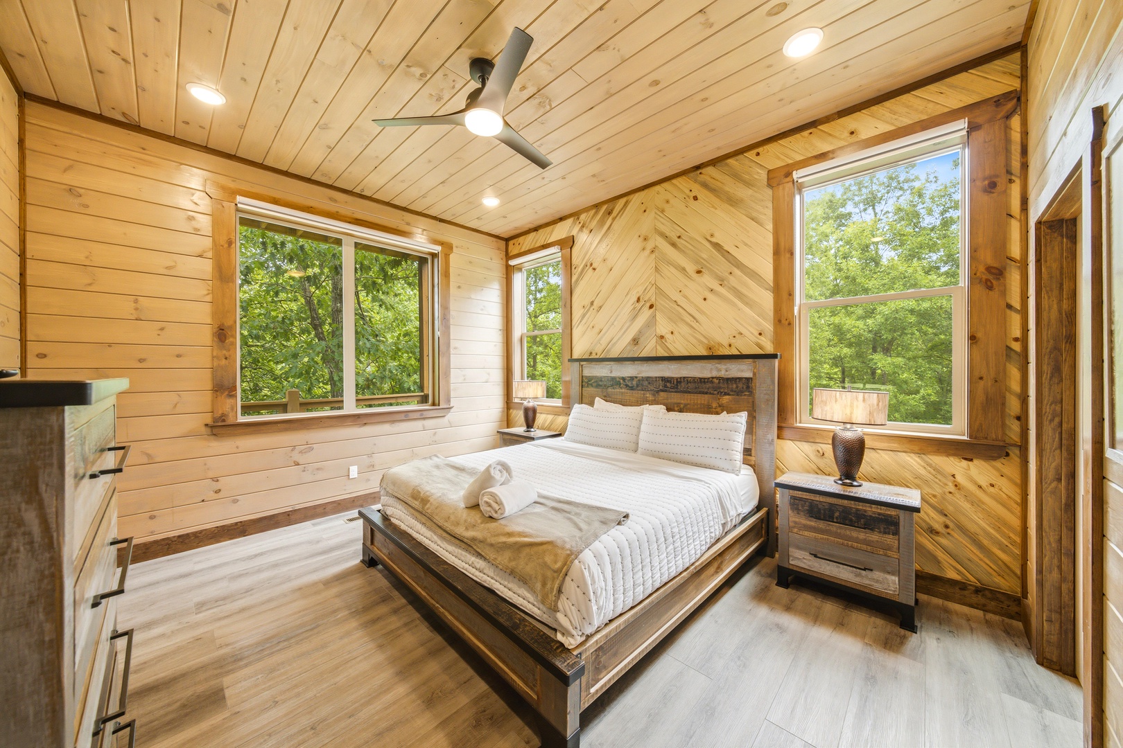 Wake up to soft sunlight streaming through floor-to-ceiling windows, framing lush forest views that make you feel at one with nature. Your retreat features warm wood tones, cozy furnishings, and a ceiling fan to keep you comfortable year-round.