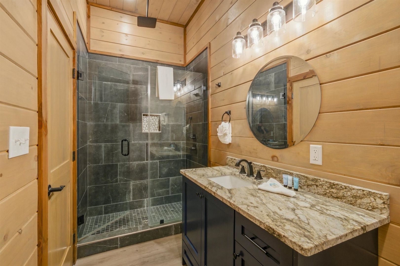 Step into your spa-like retreat with a luxurious glass-enclosed shower and elegant granite vanity, perfectly complemented by warm wood finishes.