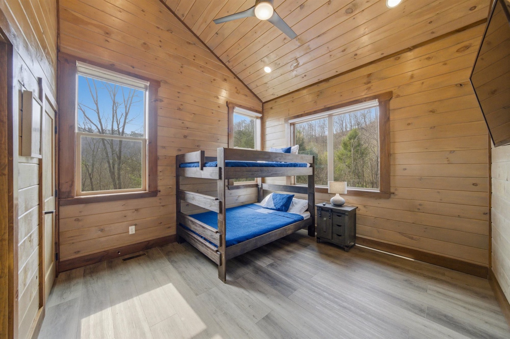 Cozy cabin bedroom with rustic wood walls where you'll sleep soundly on bunk beds while enjoying peaceful forest views.