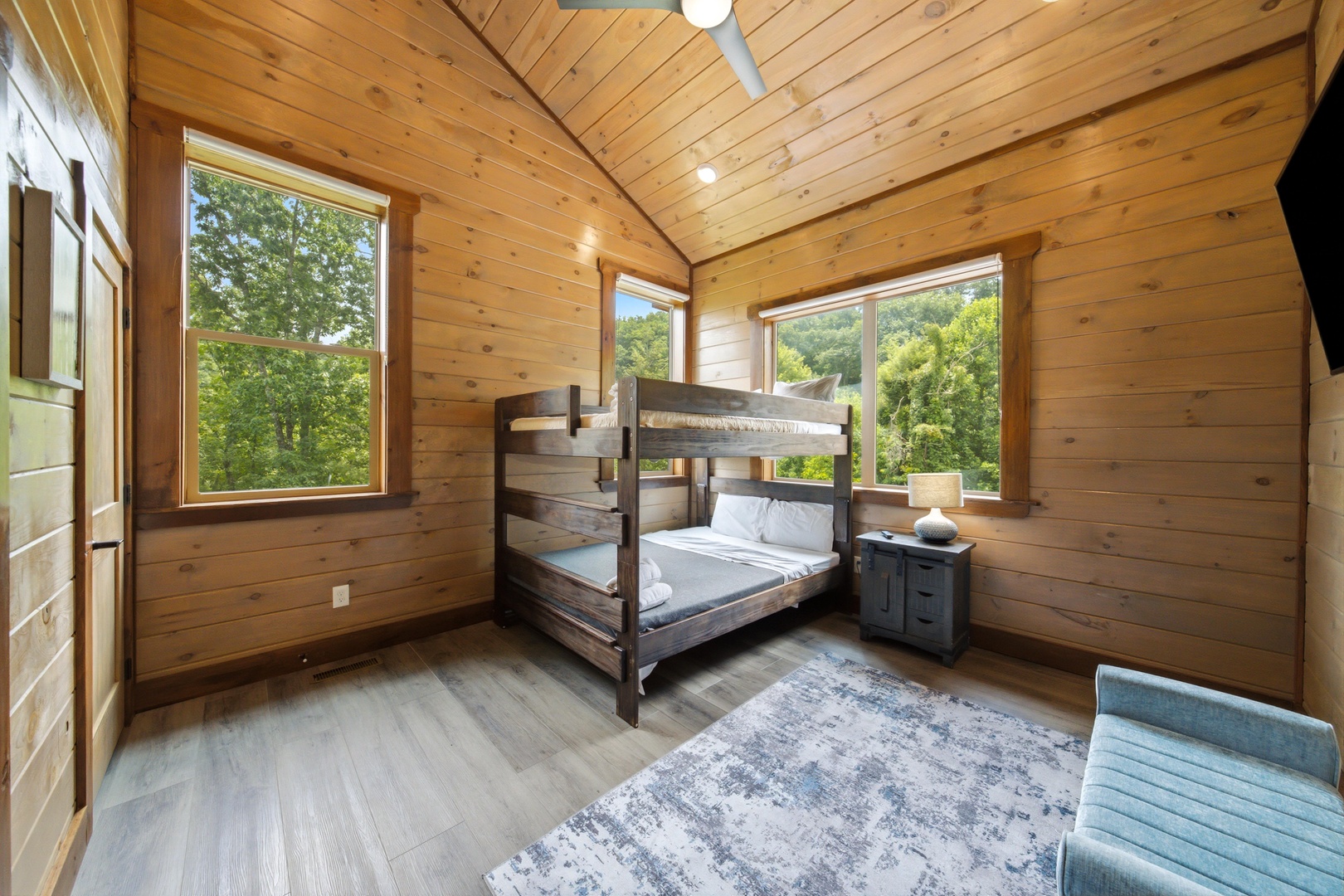 Rest easy in this inviting bunk room, where warm wood tones and sunlight filtering through large windows create your perfect retreat. Natural greenery surrounds you, making every moment peaceful.