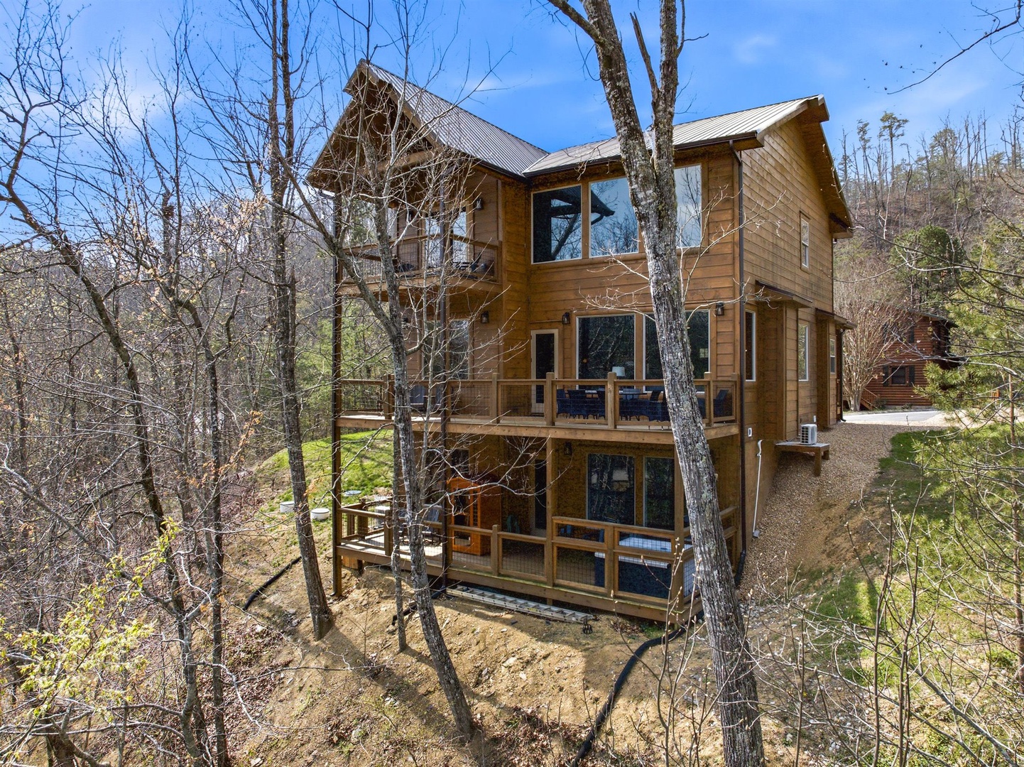 Beautiful wooden cabin nestled among towering trees, featuring multiple decks and large windows that frame the surrounding forest landscape.