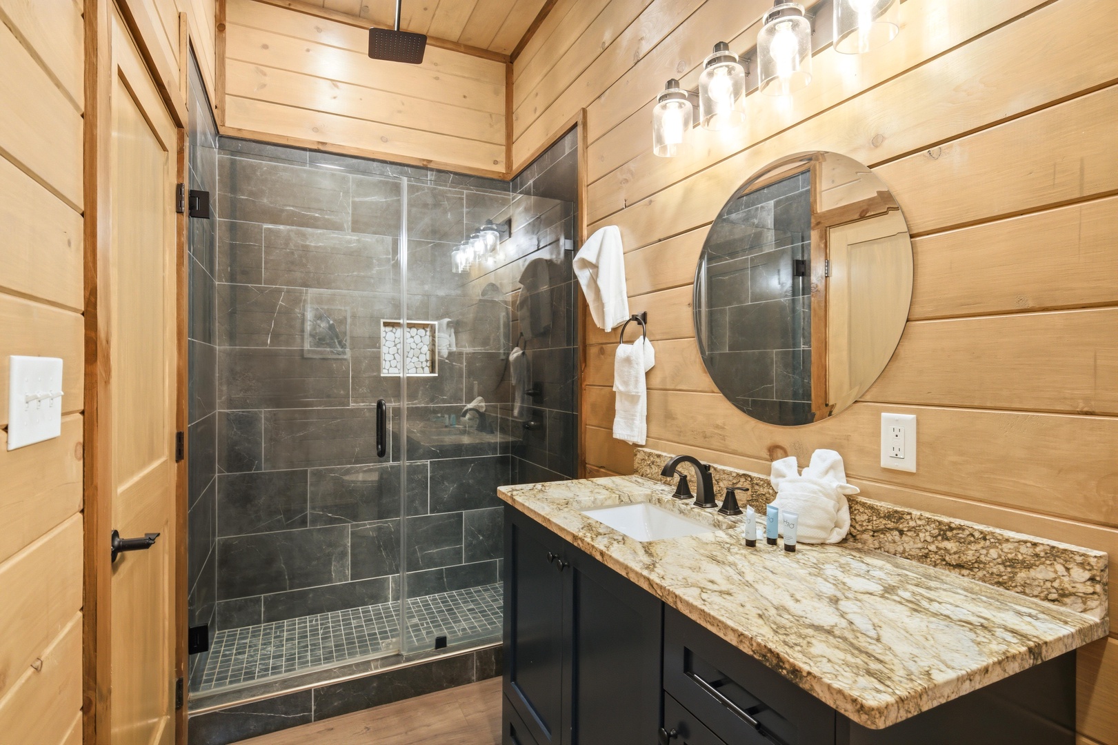 You'll love the warm shiplap walls and modern slate shower in this beautifully appointed bathroom, complete with granite counters and soft lighting.