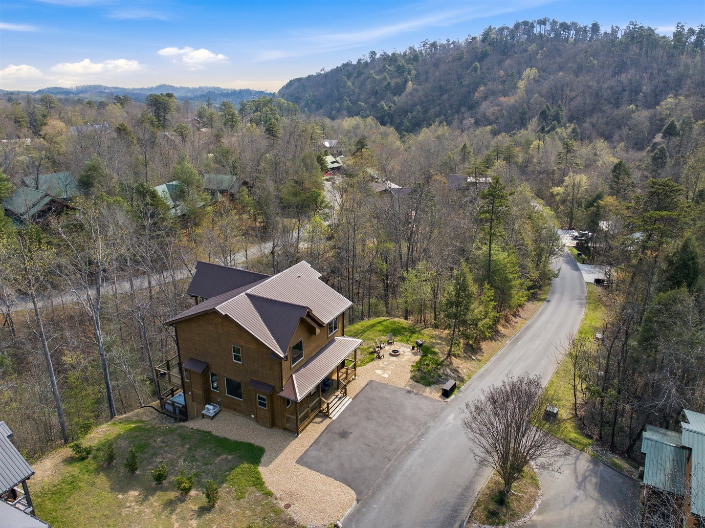 Aerial view of a mountain cabin retreat nestled among rolling hills and forested landscapes, offering a peaceful escape in nature.