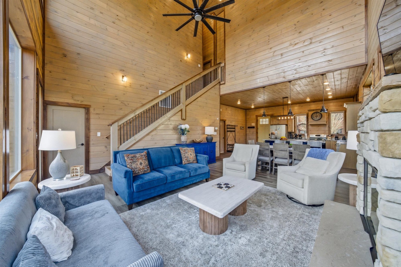 Relax in your spacious living area featuring a vibrant blue sofa, cozy seating, and stunning wood-beam ceilings that create the perfect mountain retreat atmosphere.