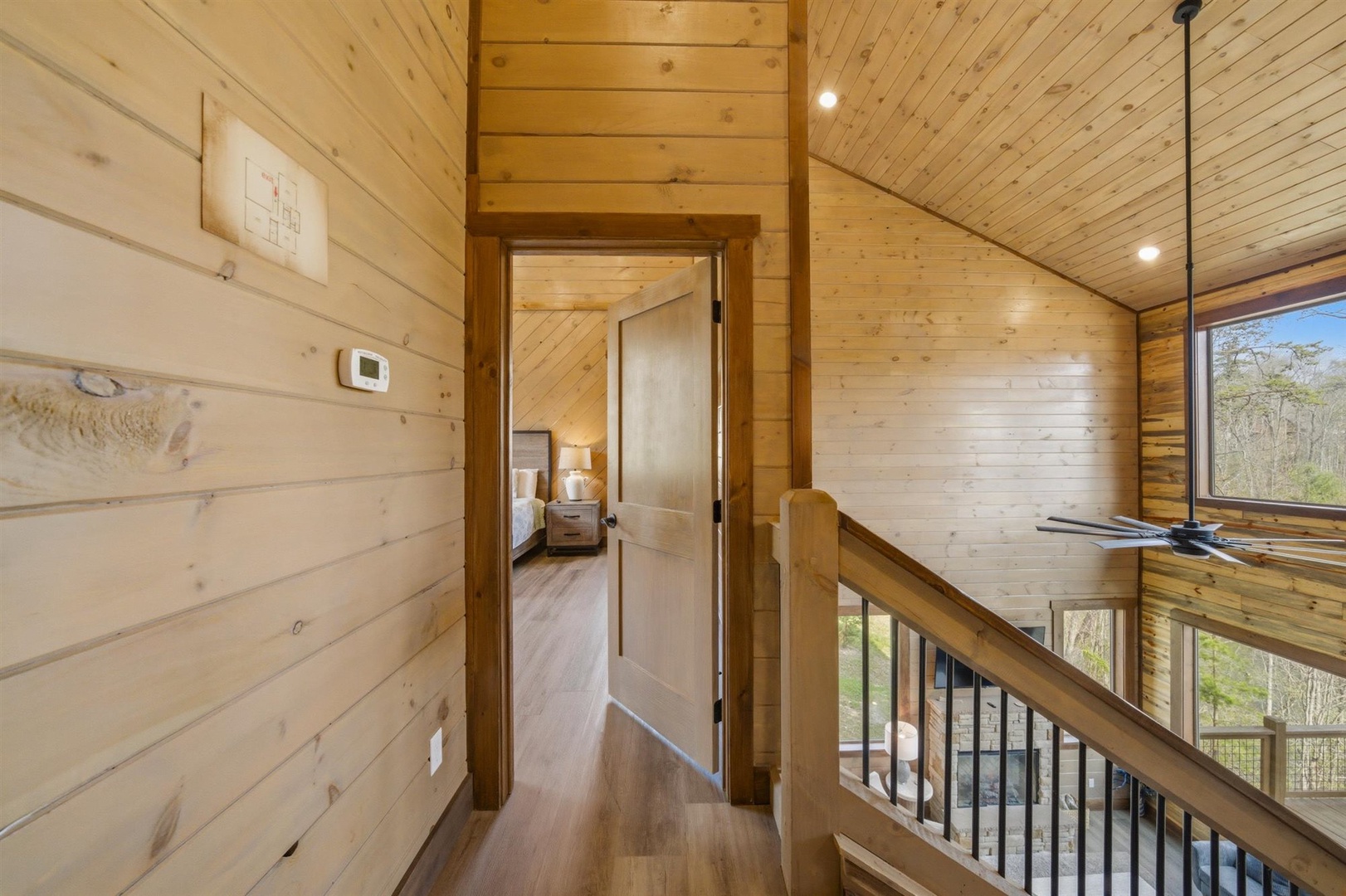 Ascend the warm wood staircase where natural light floods through tall windows, revealing glimpses of your peaceful bedroom retreat ahead.