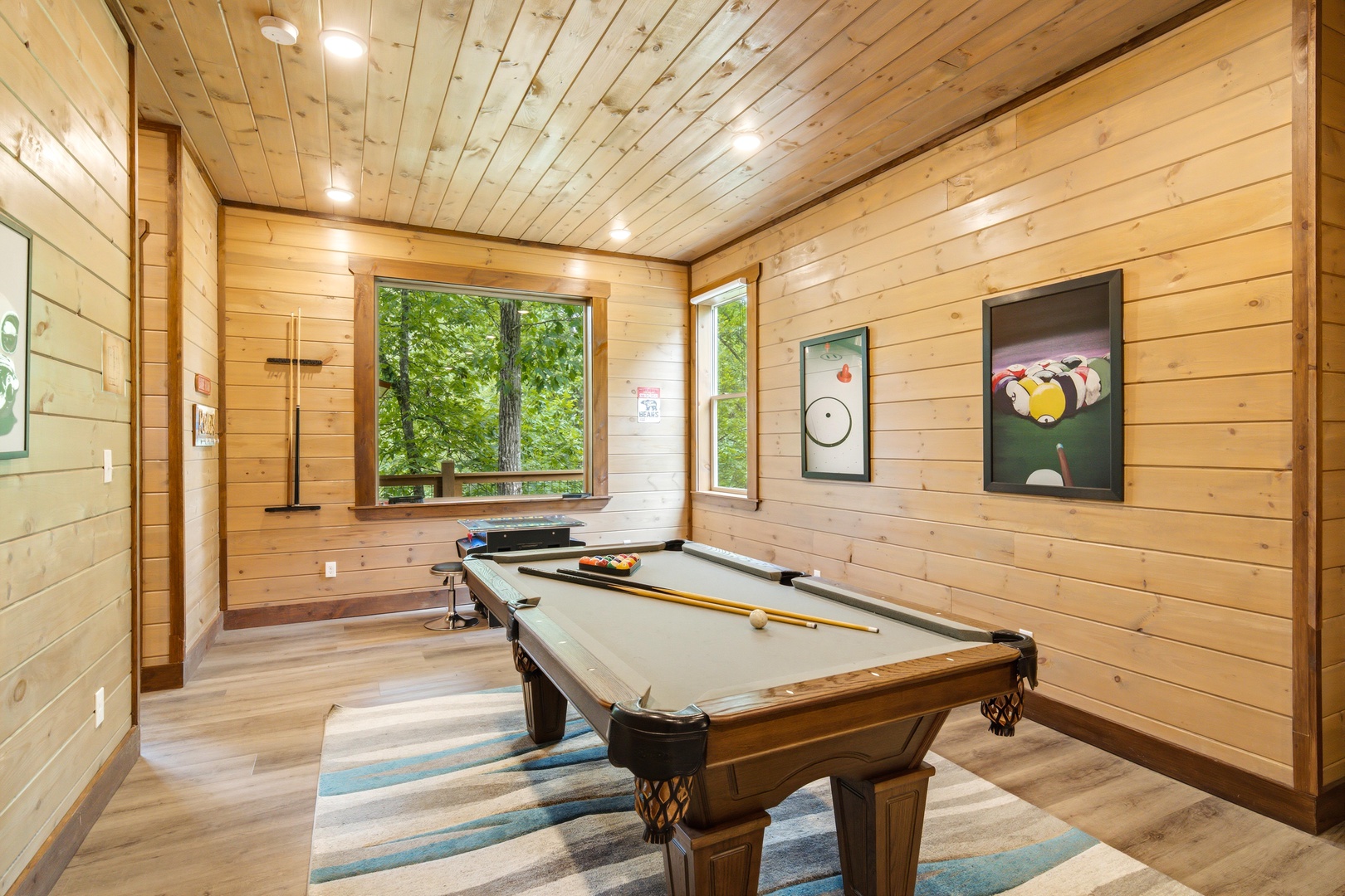 Challenge your friends to a game in this warm, wood-paneled game room with a tournament-ready pool table, surrounded by natural light and forest views.