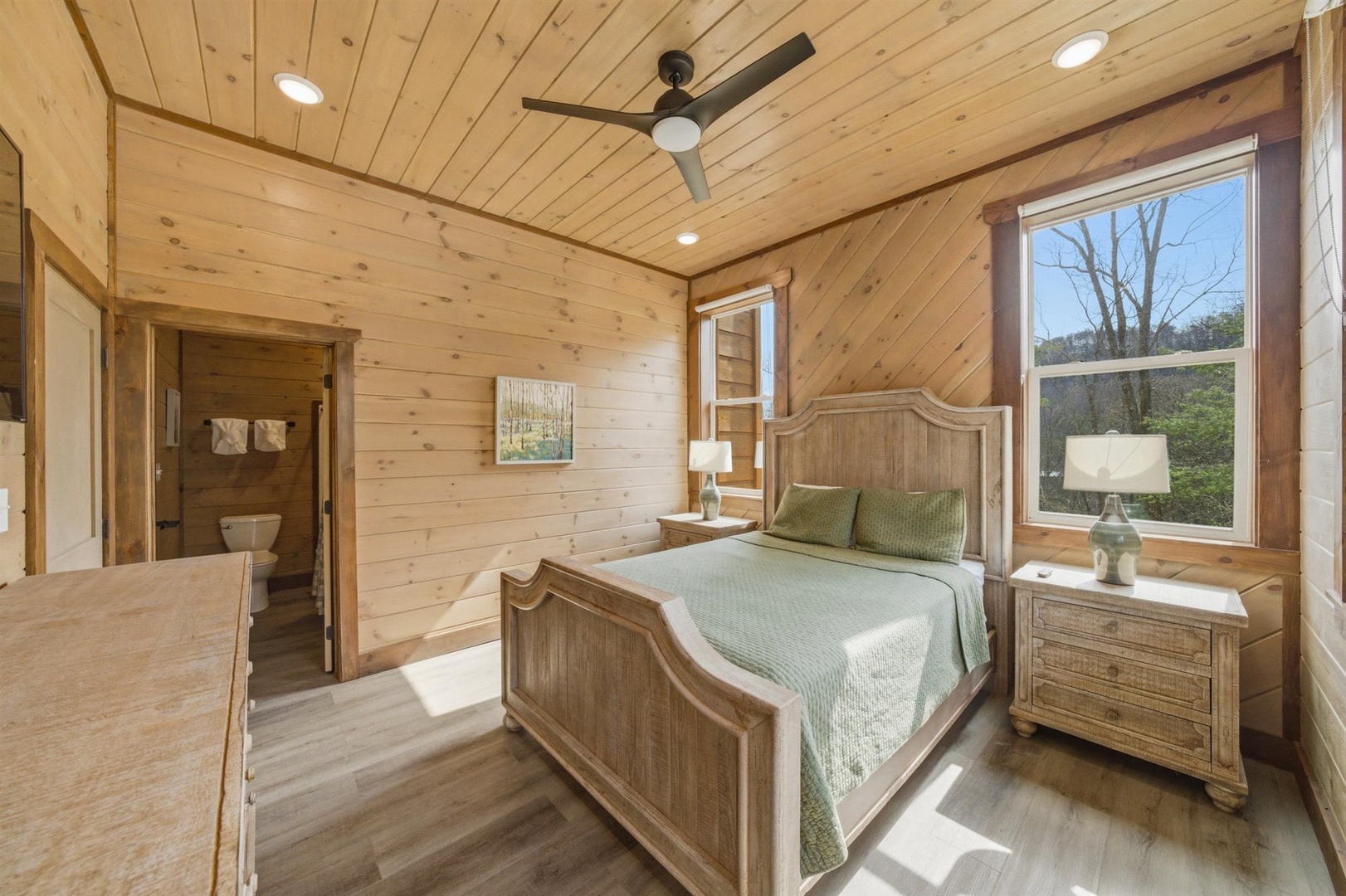 Rest peacefully in your cozy bedroom featuring warm wood walls, comfortable furnishings, and natural light streaming through large windows.