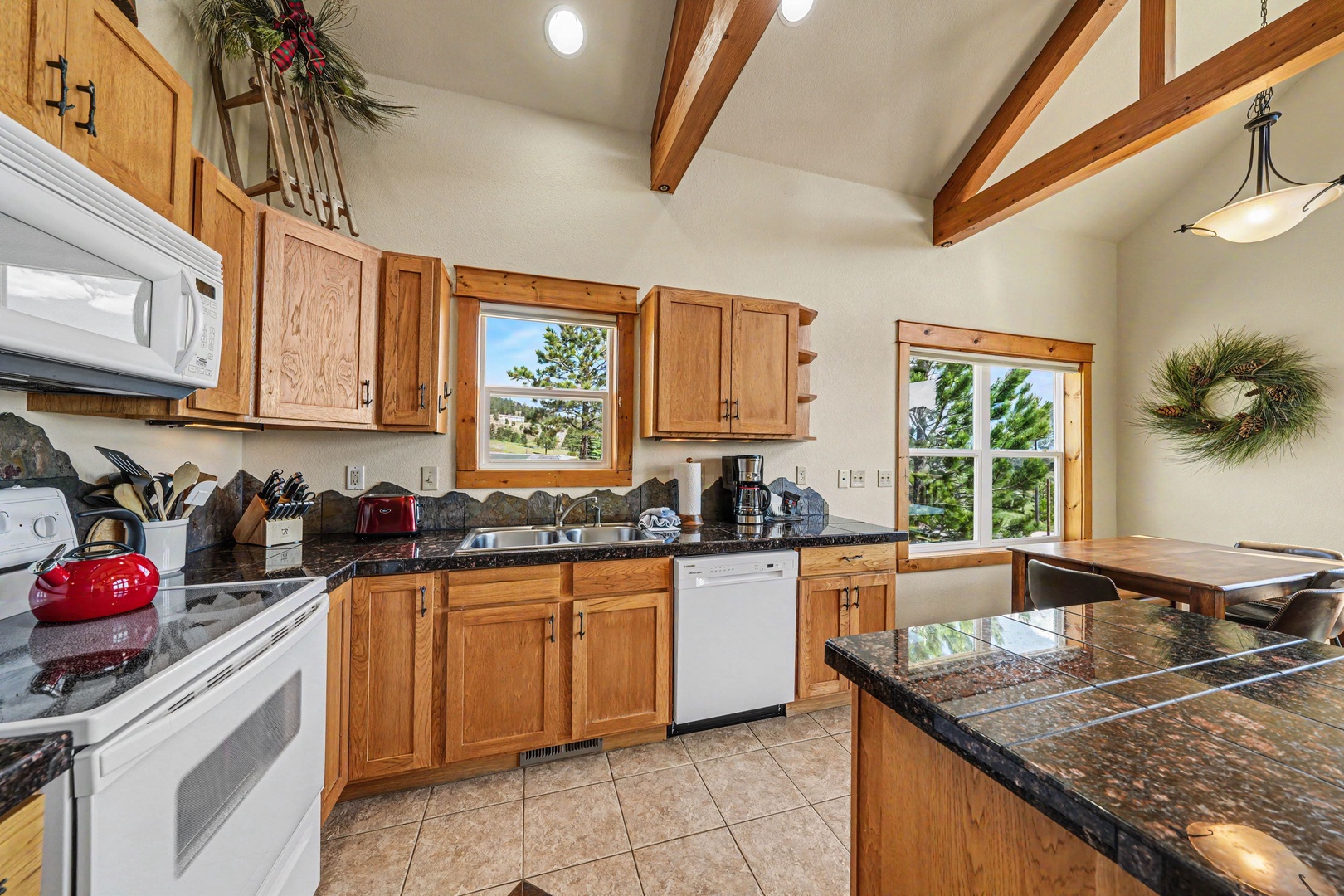 Your fully equipped kitchen features rich wood cabinetry, granite countertops, and vaulted ceilings with exposed beams, creating a warm and welcoming space to prepare meals with mountain views framing the windows.