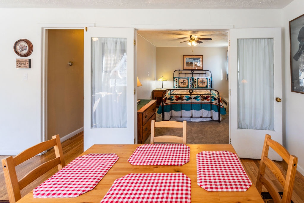 Step into your cozy dining space where cheerful gingham placemats await family meals, with another comfortable bedroom just beyond.