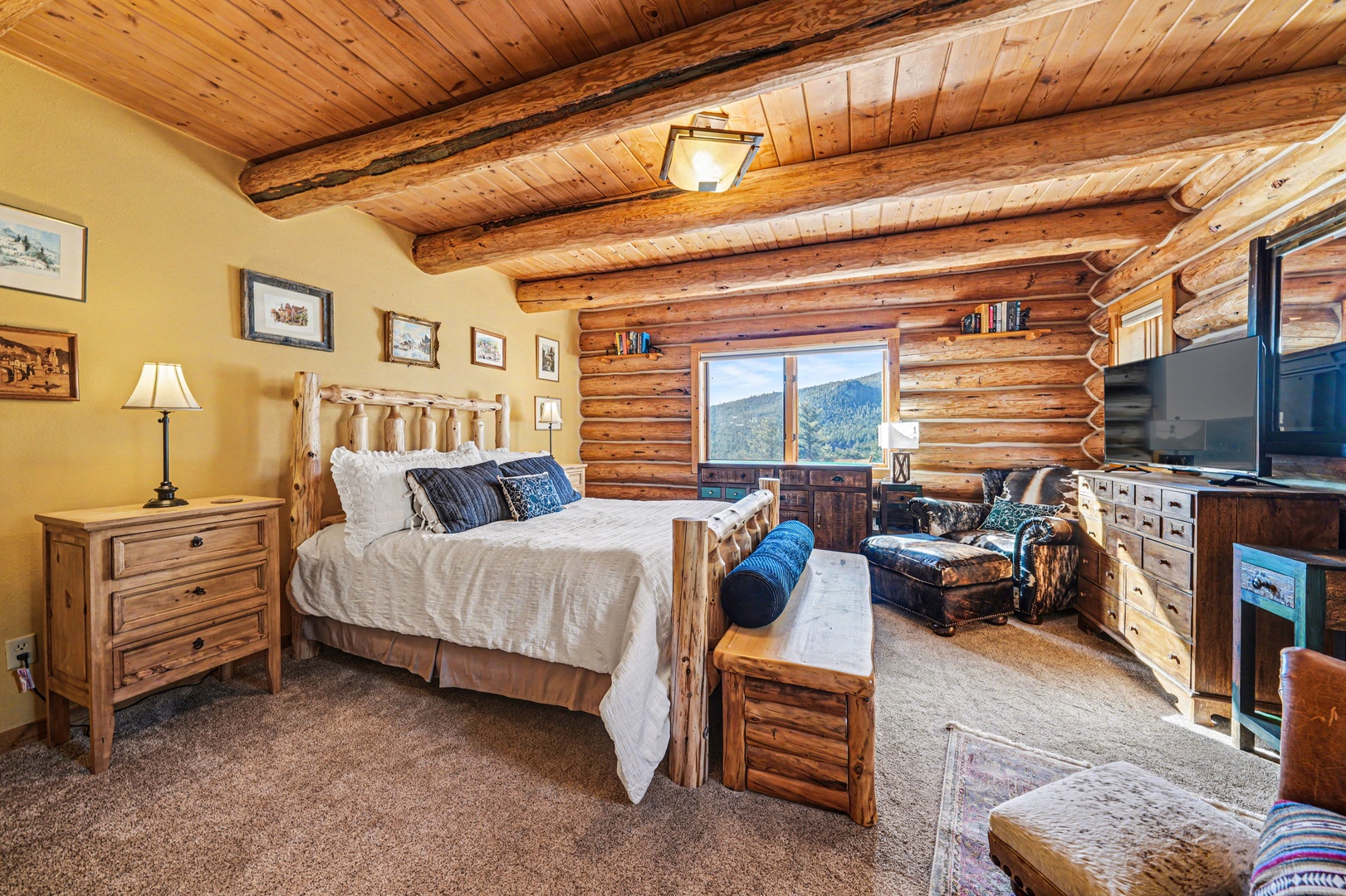 Cozy log cabin bedroom where rustic charm meets mountain views. Unwind in comfort with exposed beam ceilings overhead.