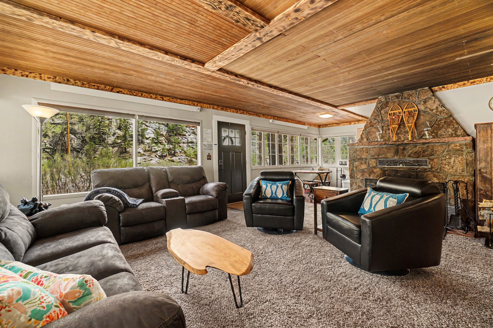 Relax in comfort with plush seating and stunning river views through floor-to-ceiling windows. The rustic wood-beam ceiling and stone fireplace create a warm, inviting retreat for your mountain getaway.