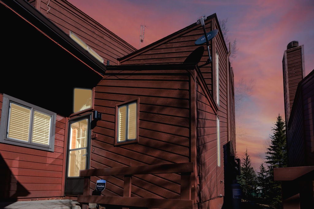 A rustic wood-sided property glows warmly against dramatic sunset skies, creating a welcoming atmosphere in this mountain setting.