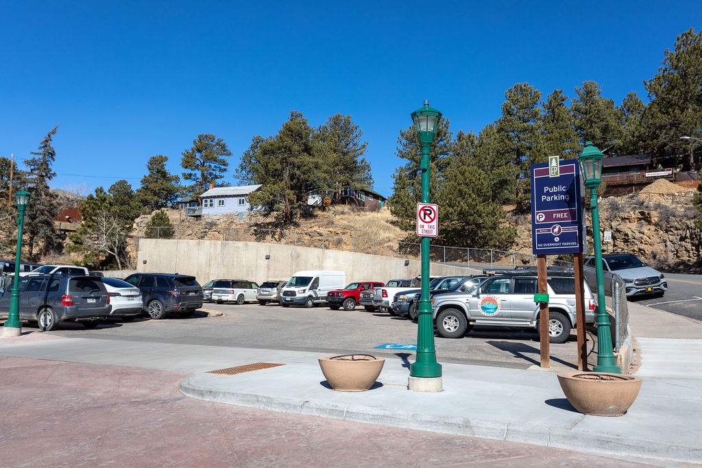 Public parking area surrounded by natural landscape and residential buildings in a scenic mountain setting.