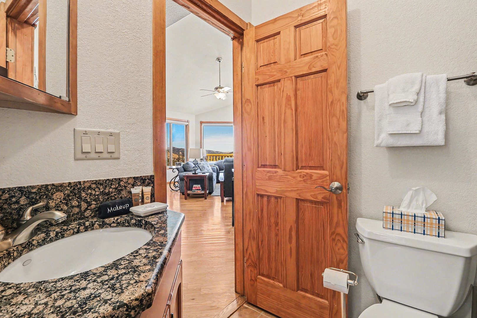 Full bathroom features granite counters, warm wood accents, and fresh towels, creating a comfortable retreat.