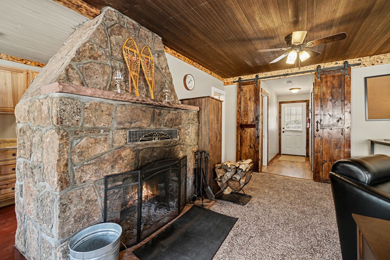 Cozy up by your rustic stone fireplace under warm wood-paneled ceilings, where vintage snowshoes and barn doors add mountain charm to your inviting retreat.