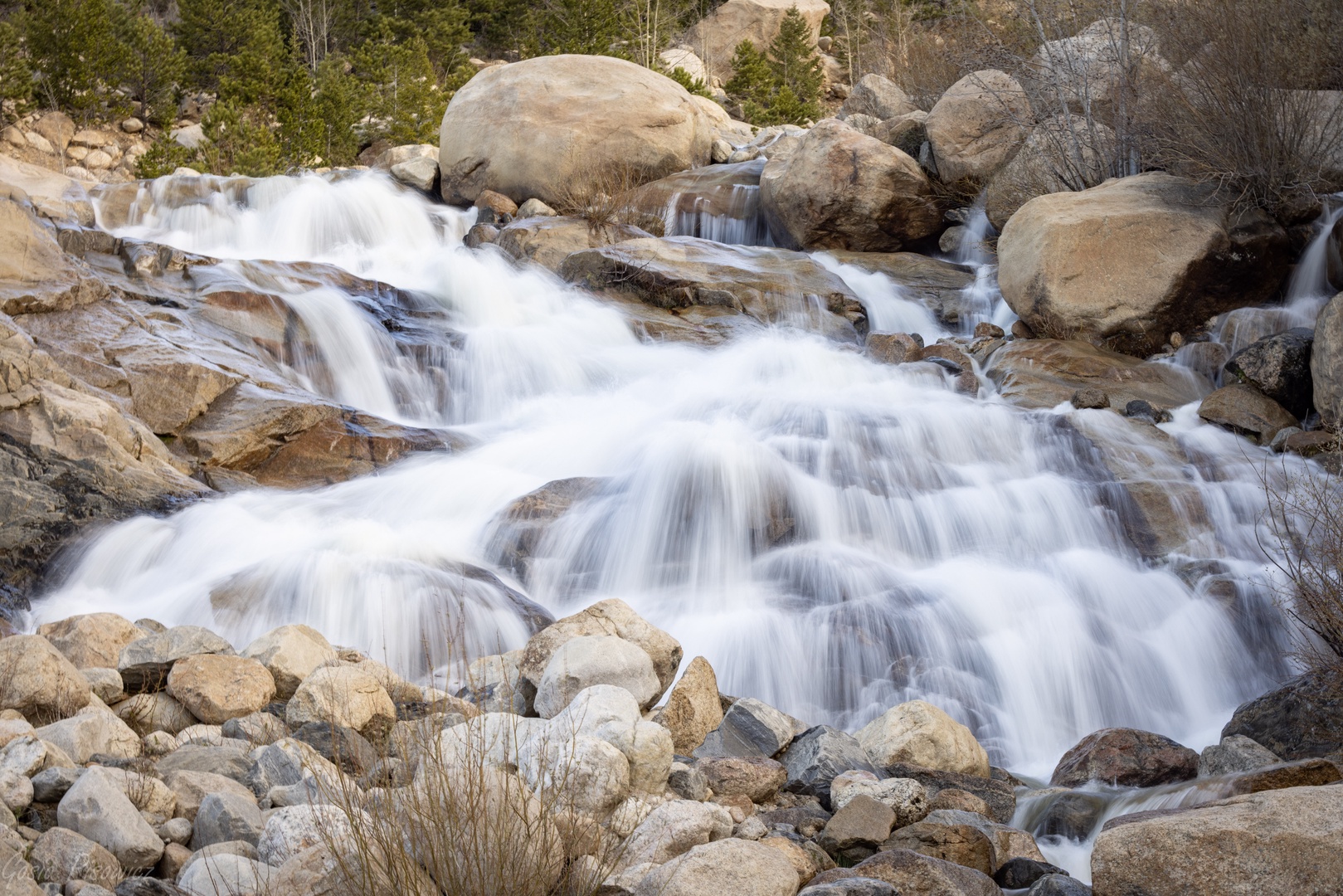 Cascading waterfall flows through granite boulders, creating a serene natural landmark in the surrounding area.