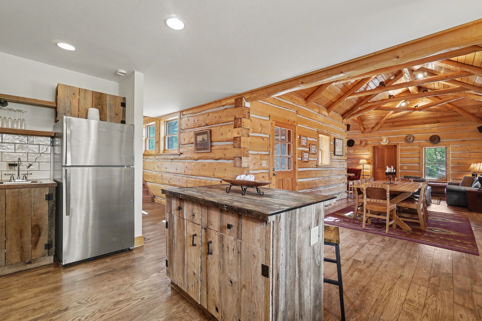 Step into your rustic retreat where exposed log beams frame an open-concept living space with modern kitchen and cozy dining area.
