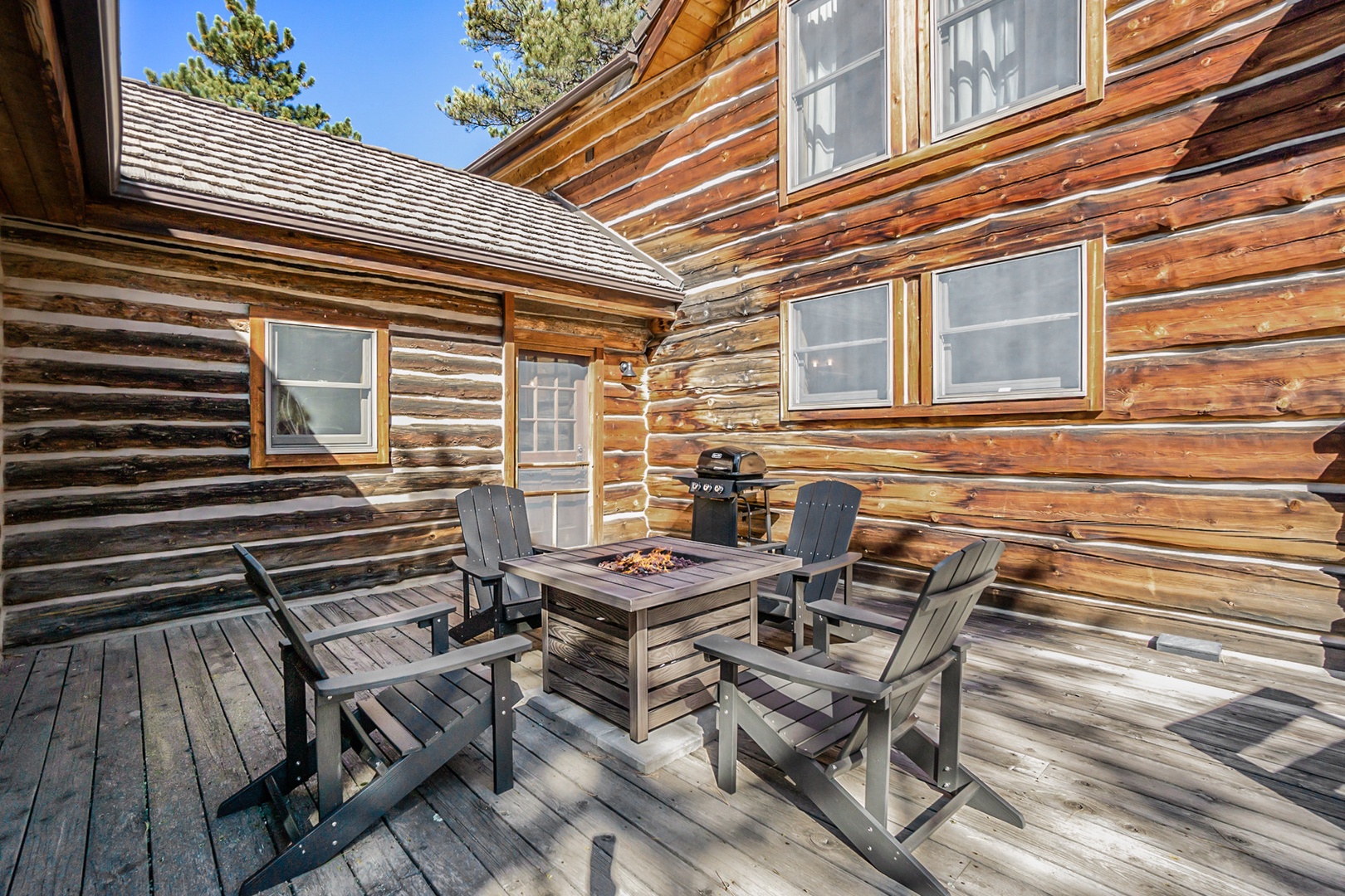 Deck with adirondack chairs around a gas fire pit. Propane grill 