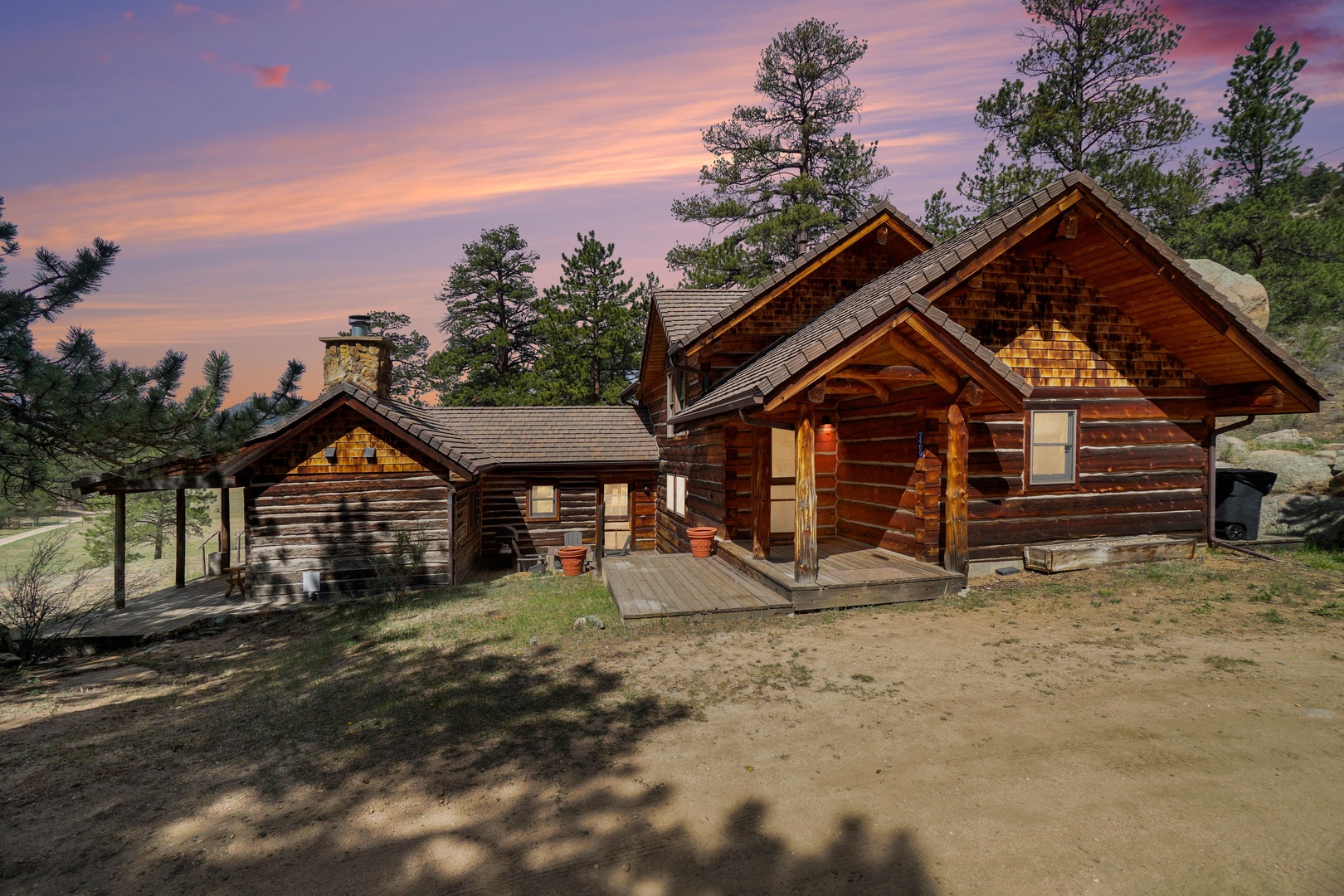 Rustic log cabin retreat nestled among towering pines under a breathtaking sunset sky.