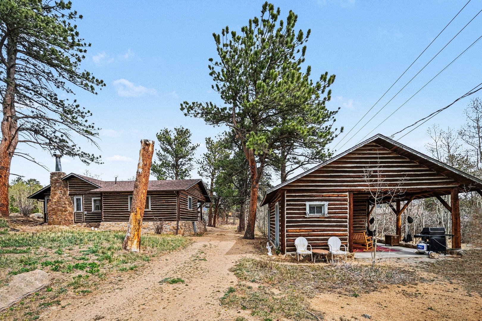 Rustic log cabin retreat nestled among towering pine trees with spacious covered pavilion for outdoor relaxation.