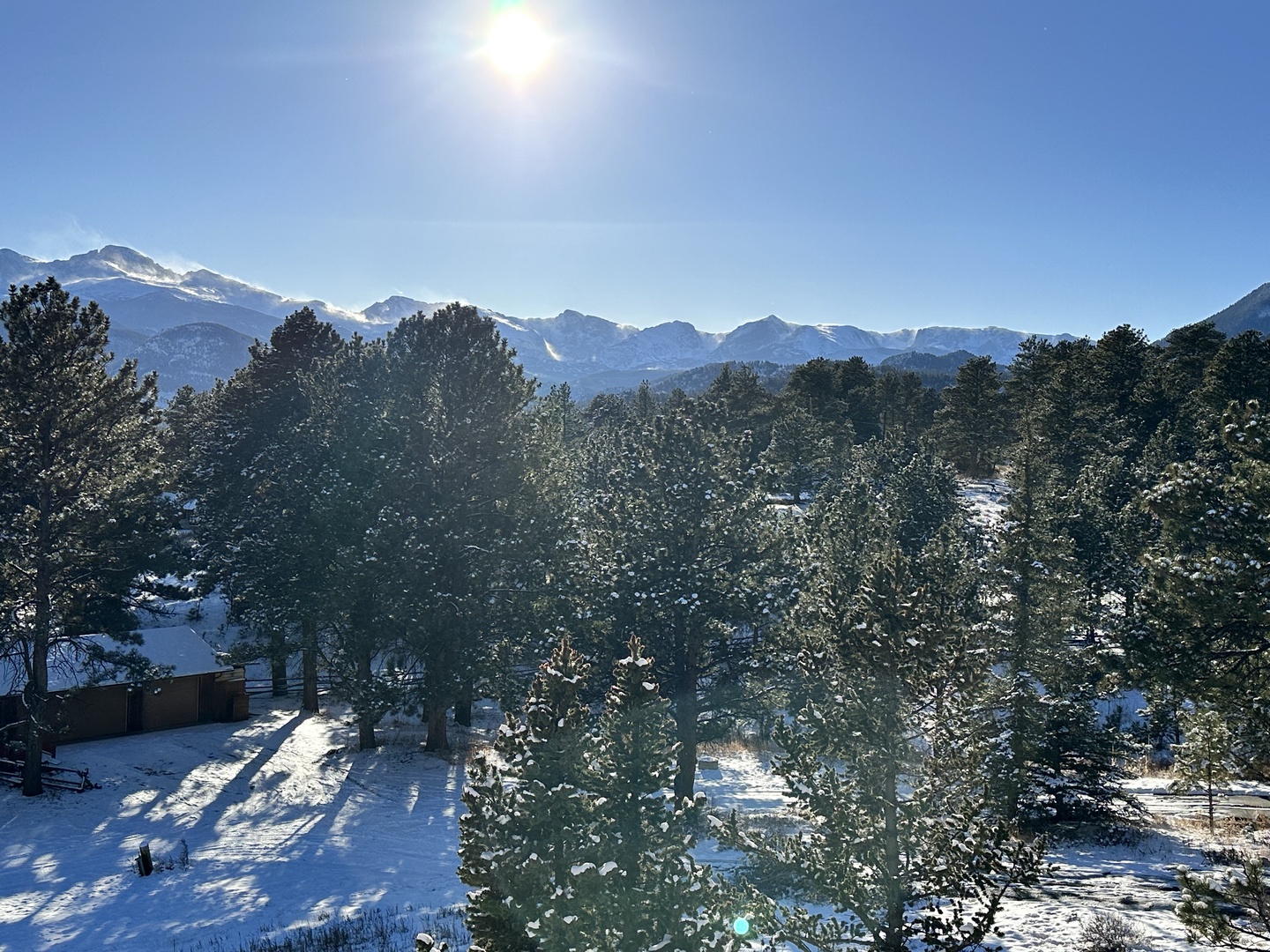 Stunning panoramic mountain view with snow-capped peaks stretching across the horizon, surrounded by peaceful forested landscape.