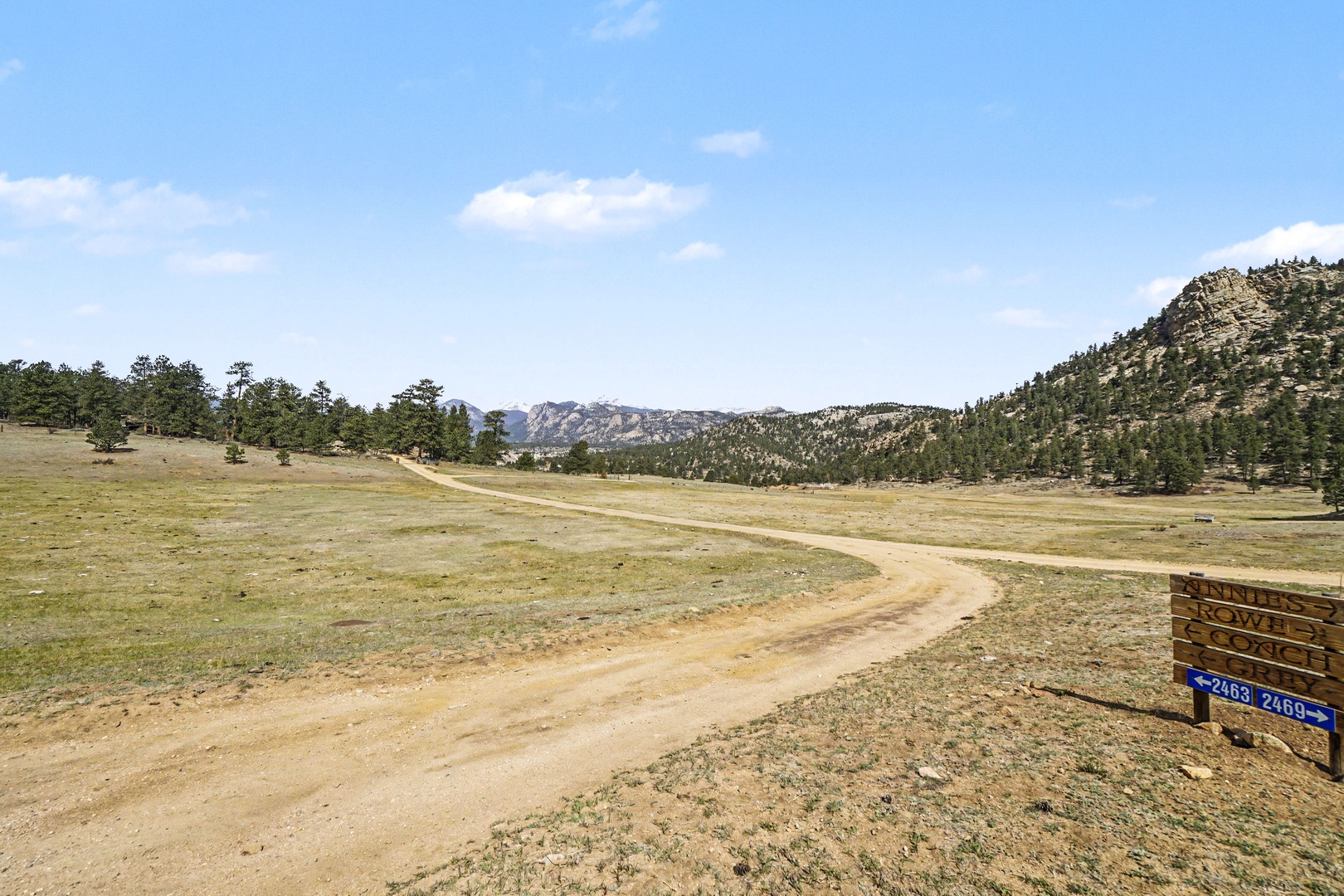 A winding dirt road leads through open countryside toward forested hills and distant mountains, offering scenic rural access.