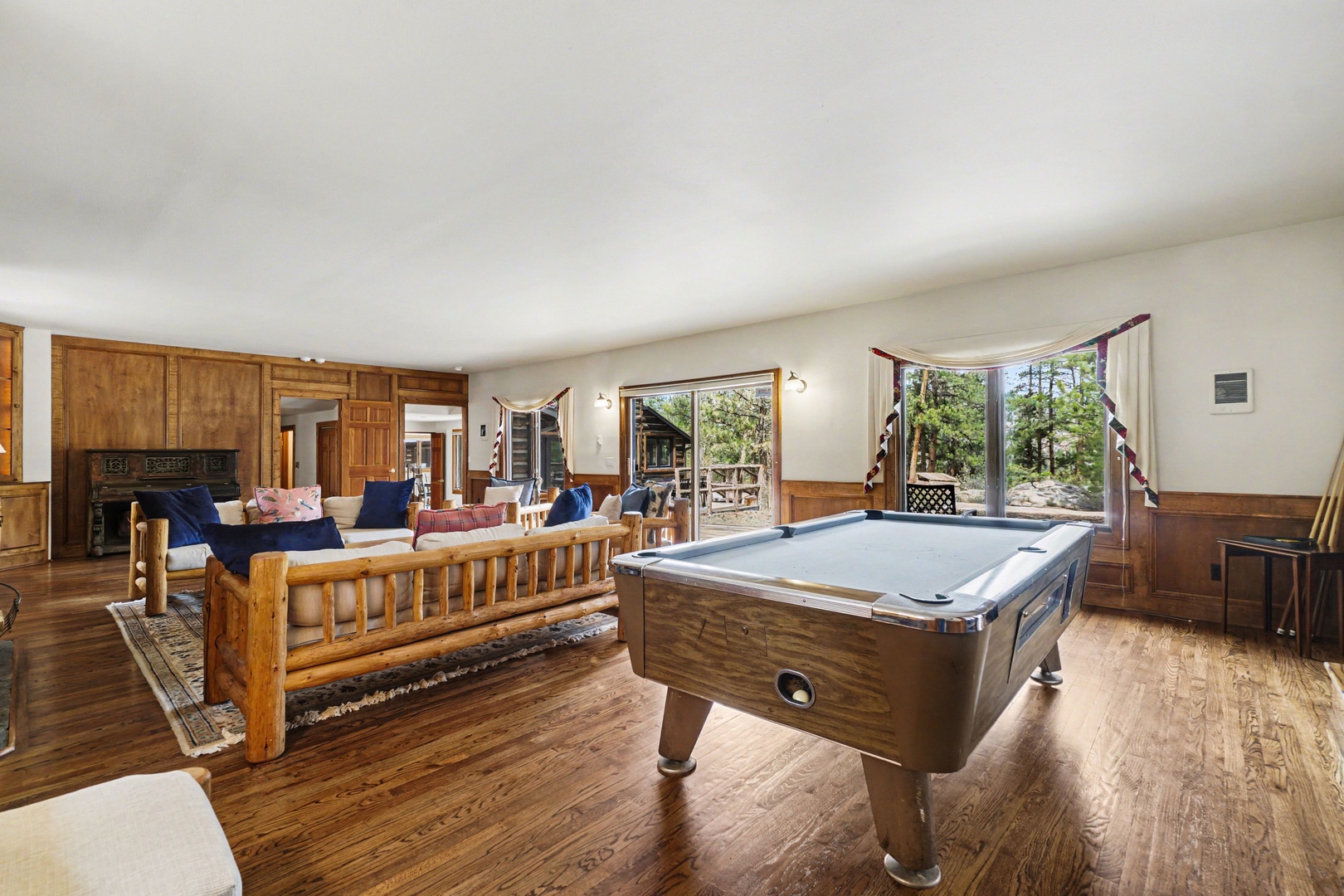 Your perfect game room awaits with a pool table and cozy seating overlooking peaceful forest views through expansive windows.