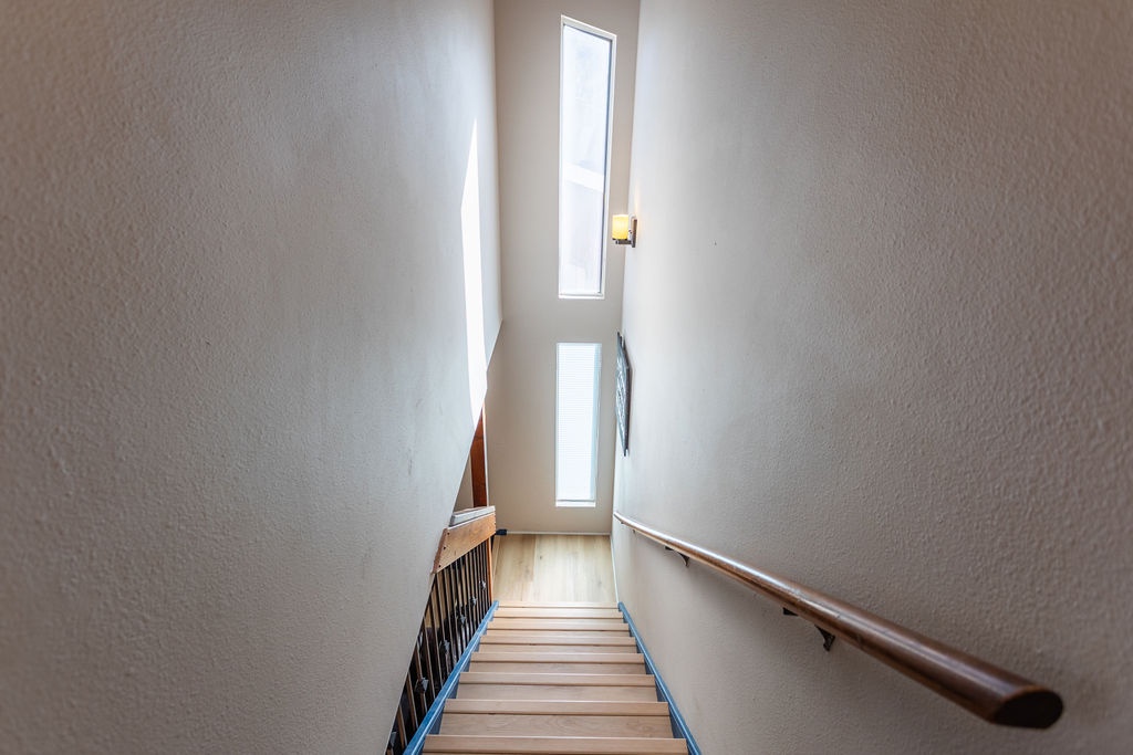 Your bright stairway leads you to comfort, with natural light streaming through tall windows and a warm wooden handrail guiding your way.