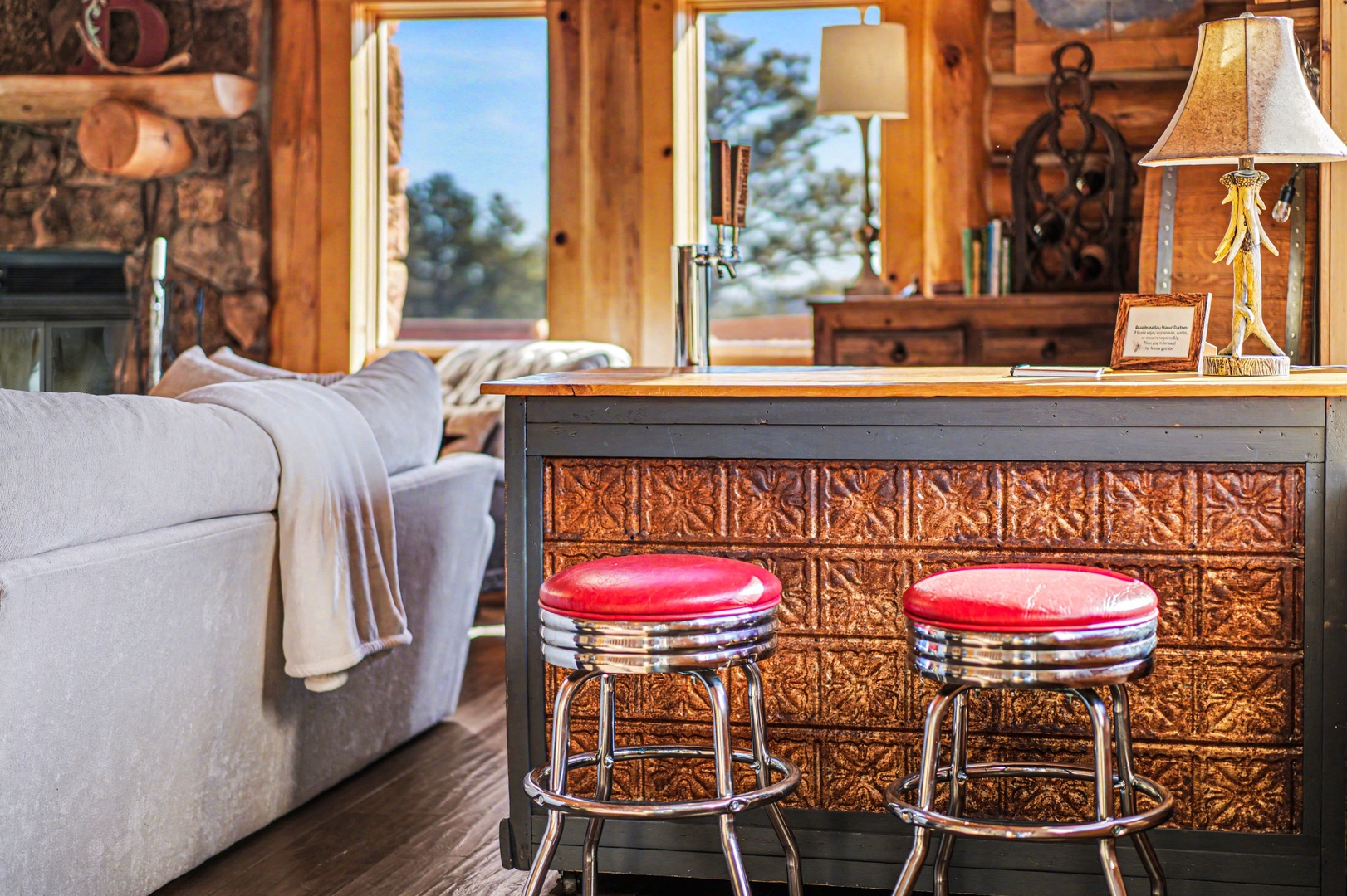 Unwind at your rustic bar with vintage red stools, where warm wood and stone create the perfect spot for evening conversations.