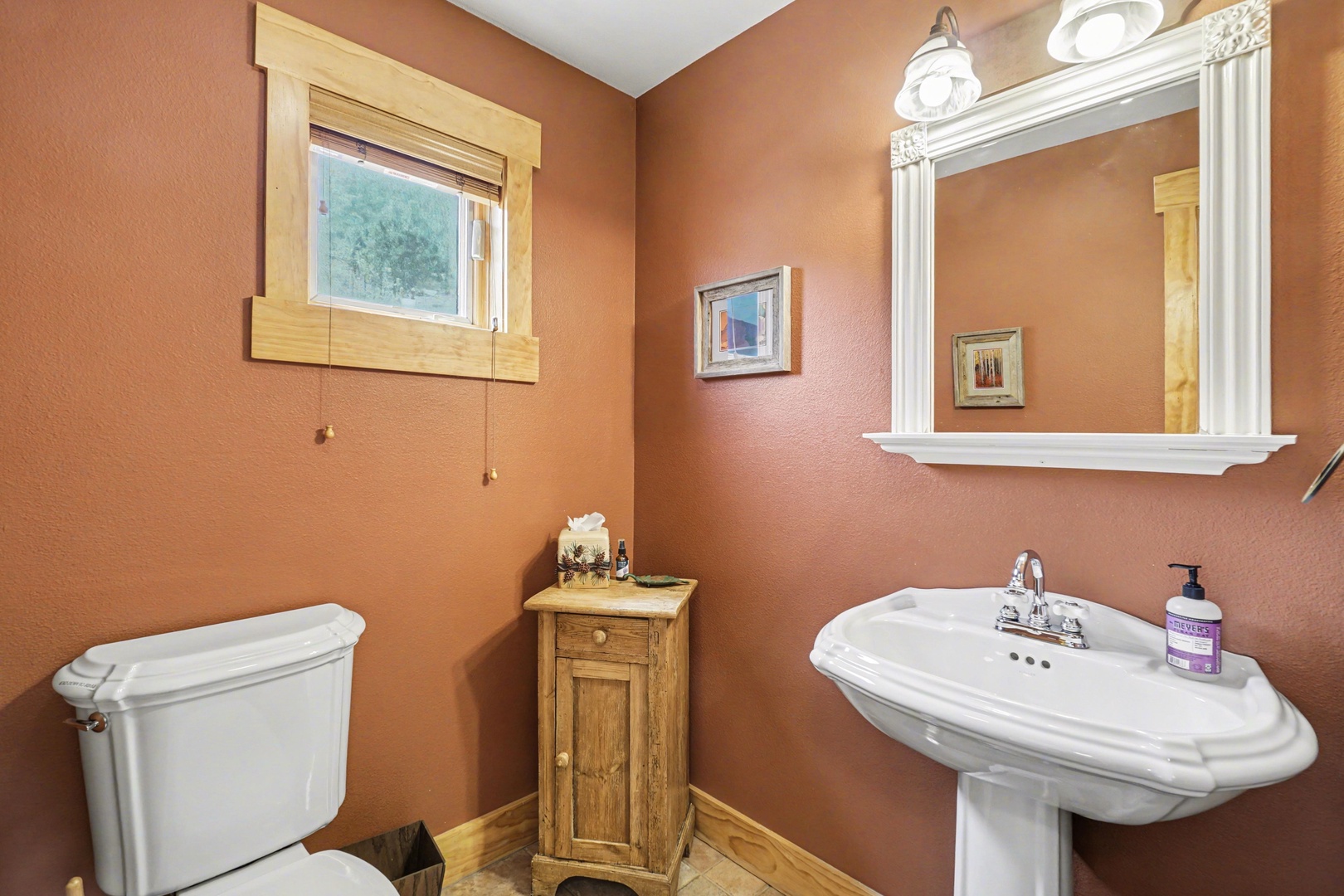 Refresh in your private powder room featuring warm terracotta walls, classic pedestal sink, and charming rustic touches.