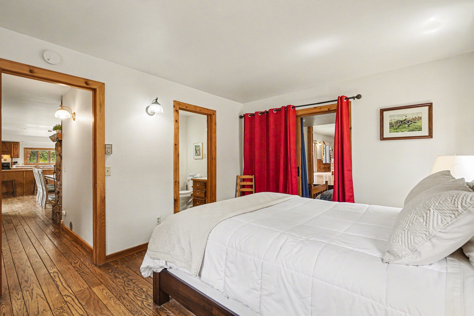 Sink into crisp linens on your comfortable bed in this charming bedroom with warm wood accents and red curtains framing peaceful views.