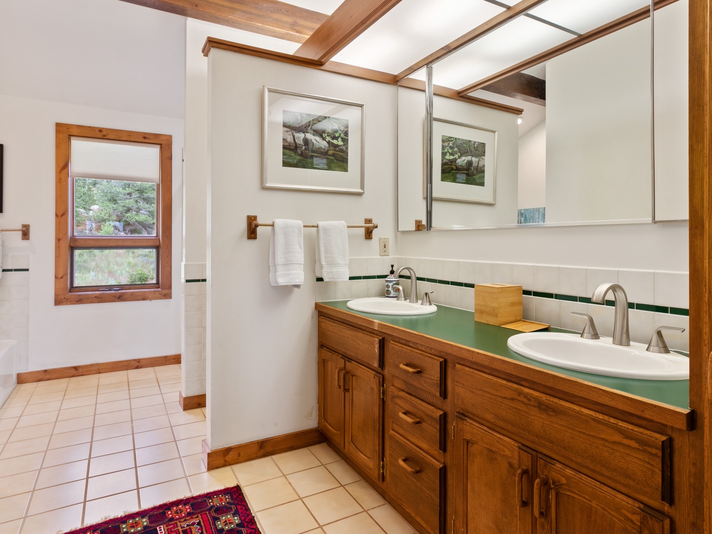 Unwind in your spacious bathroom featuring dual vanities, warm wood accents, and natural light streaming through charming windows.