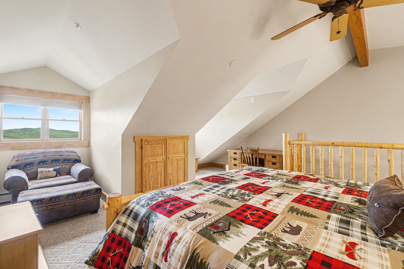 Unwind in your cozy loft bedroom with rustic charm, featuring a comfy chair and mountain views through bright windows.