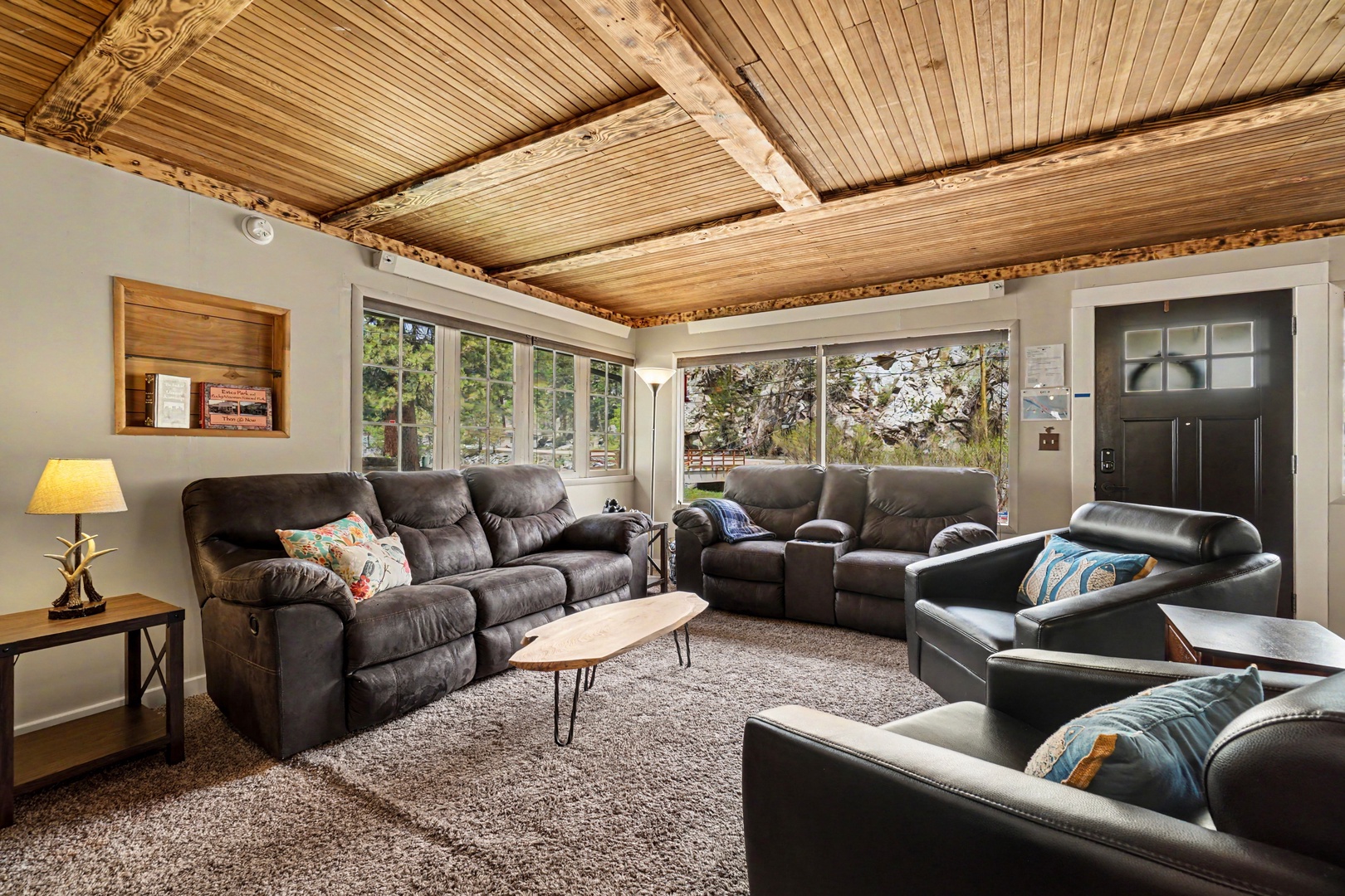 Sink into plush seating beneath soaring wood-beamed ceilings while natural light pours through expansive windows framing views of the surrounding trees and river—your perfect retreat for gathering and unwinding together.