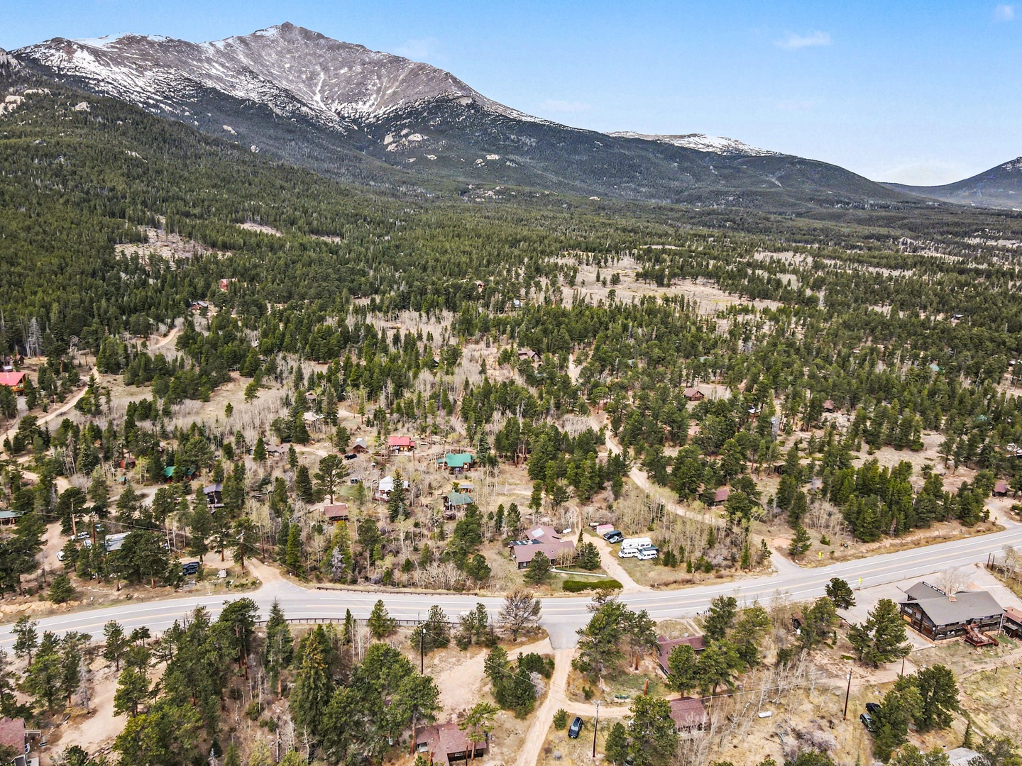 Aerial view showcasing a mountain community nestled among towering peaks and forested valleys, with residential properties scattered throughout the natural landscape.