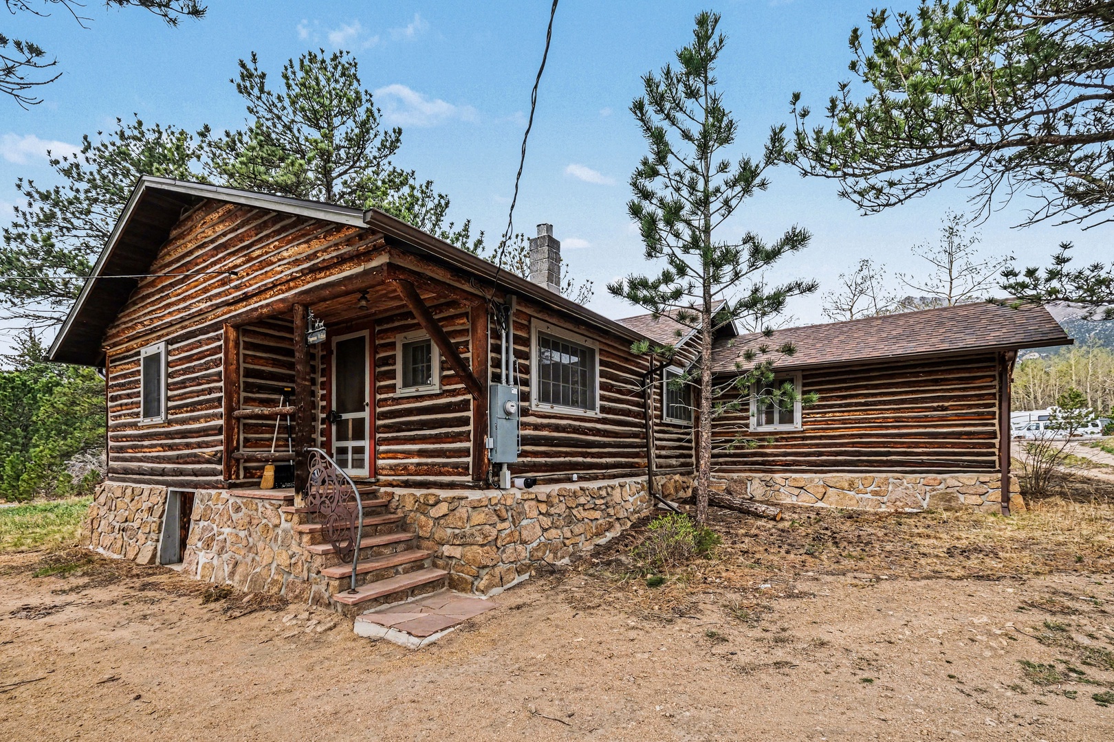 Rustic log cabin with stone foundation nestled among towering pine trees, offering authentic woodland charm and peaceful natural surroundings.