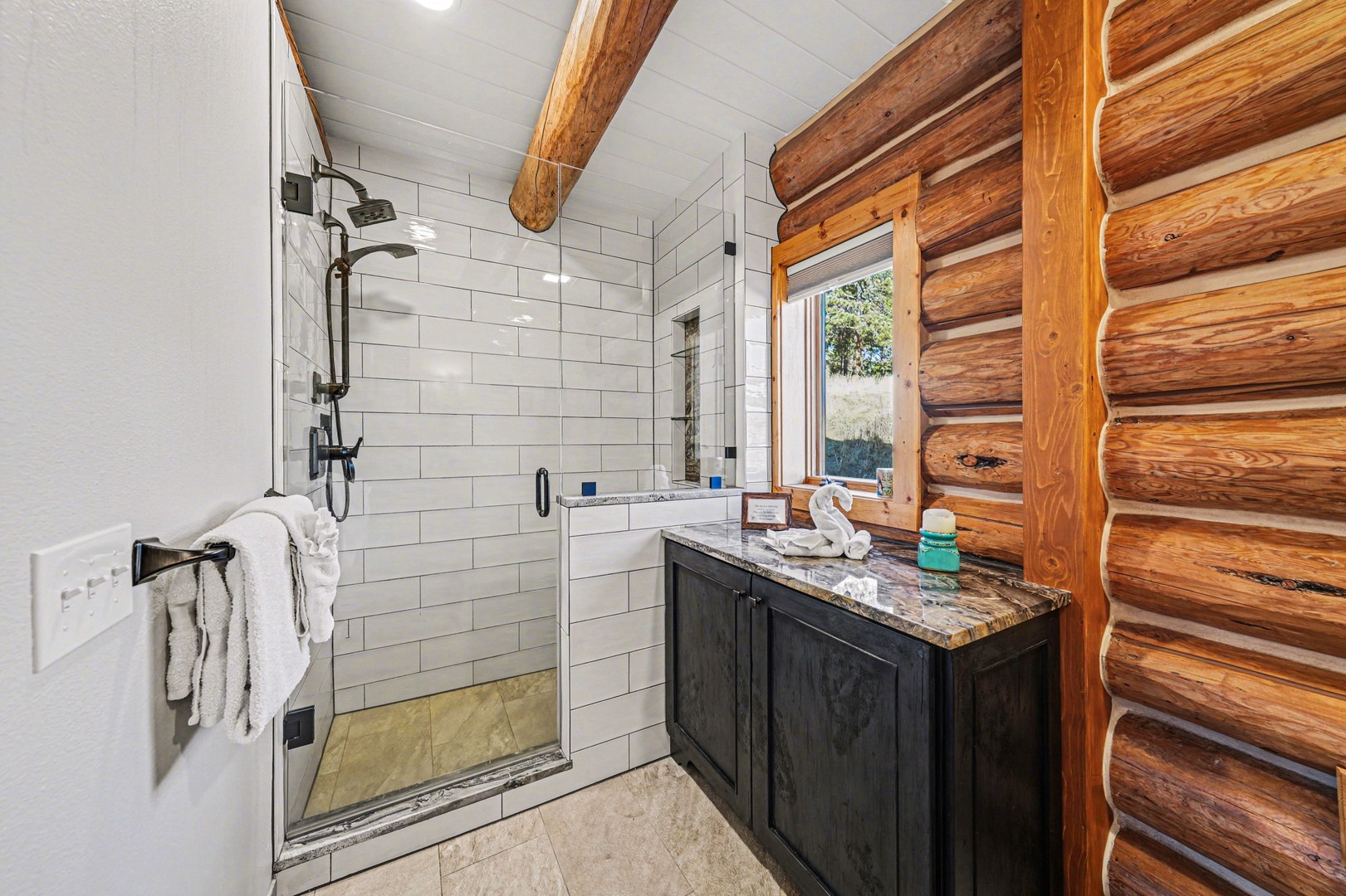 Unwind in your private bathroom featuring a spacious glass shower, rustic log cabin charm, and natural stone countertops for your mountain retreat.