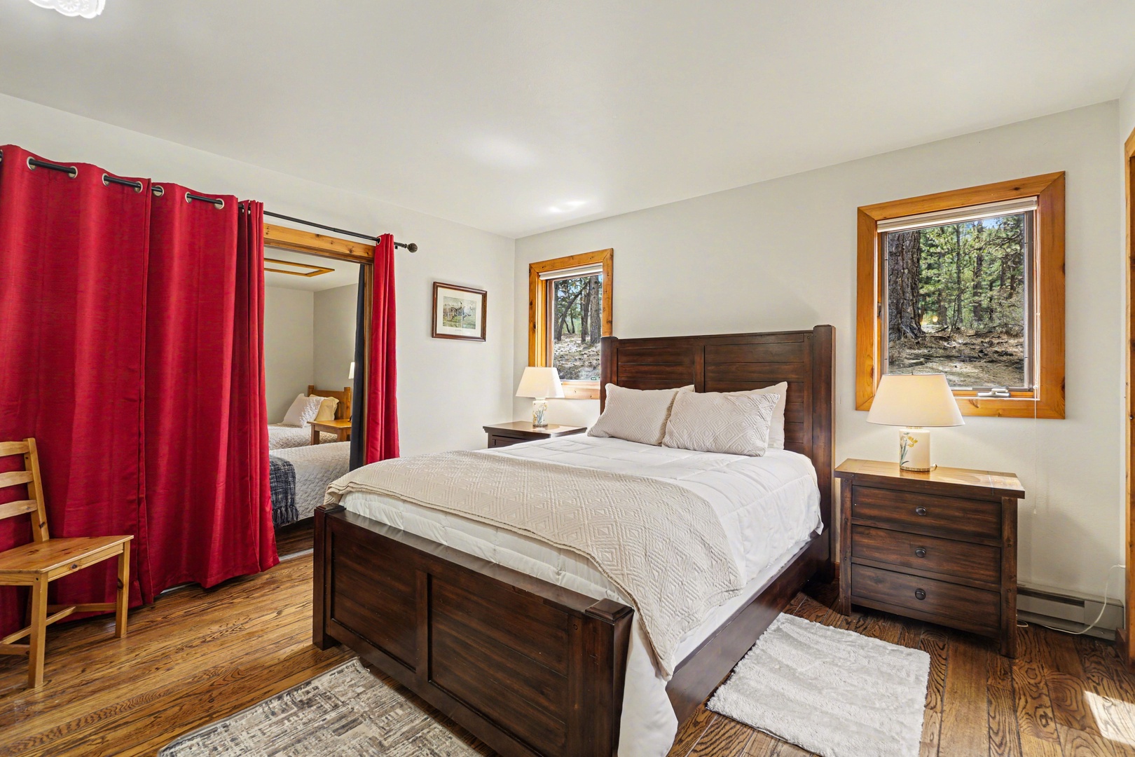 Unwind in your cozy bedroom featuring rich wood furnishings, plush bedding, and forest views through charming windows.