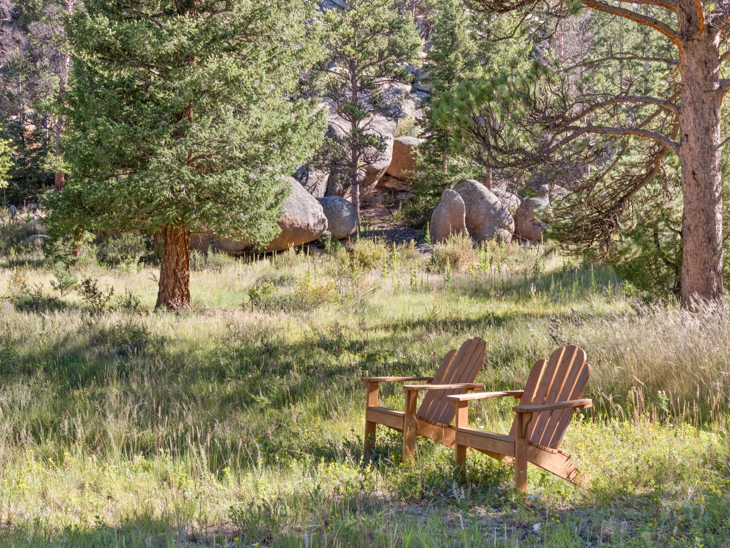Peaceful Adirondack chairs nestled among towering pines and dramatic boulder formations create a serene natural retreat.