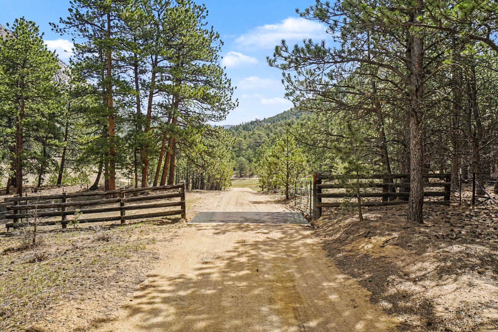 A gated entrance leads through towering pines to forested mountains, marking the arrival to this secluded mountain retreat.