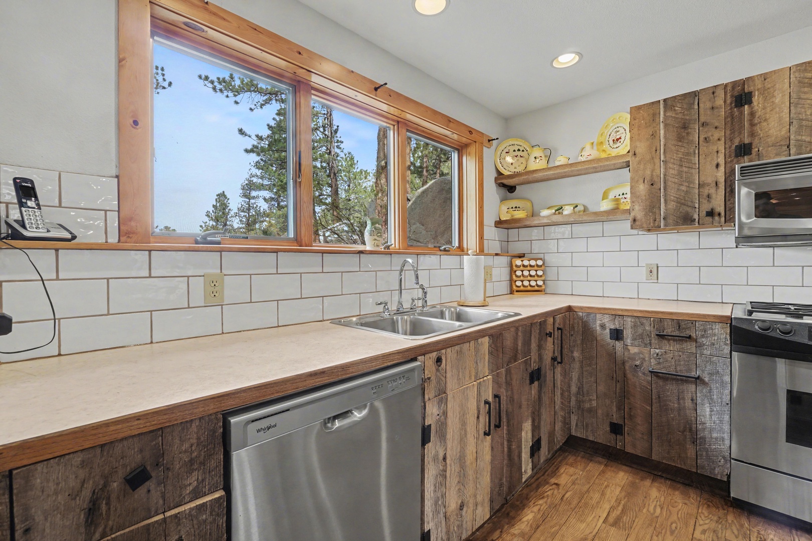 Your rustic kitchen features reclaimed wood cabinets, stainless appliances, and forest views through large windows.