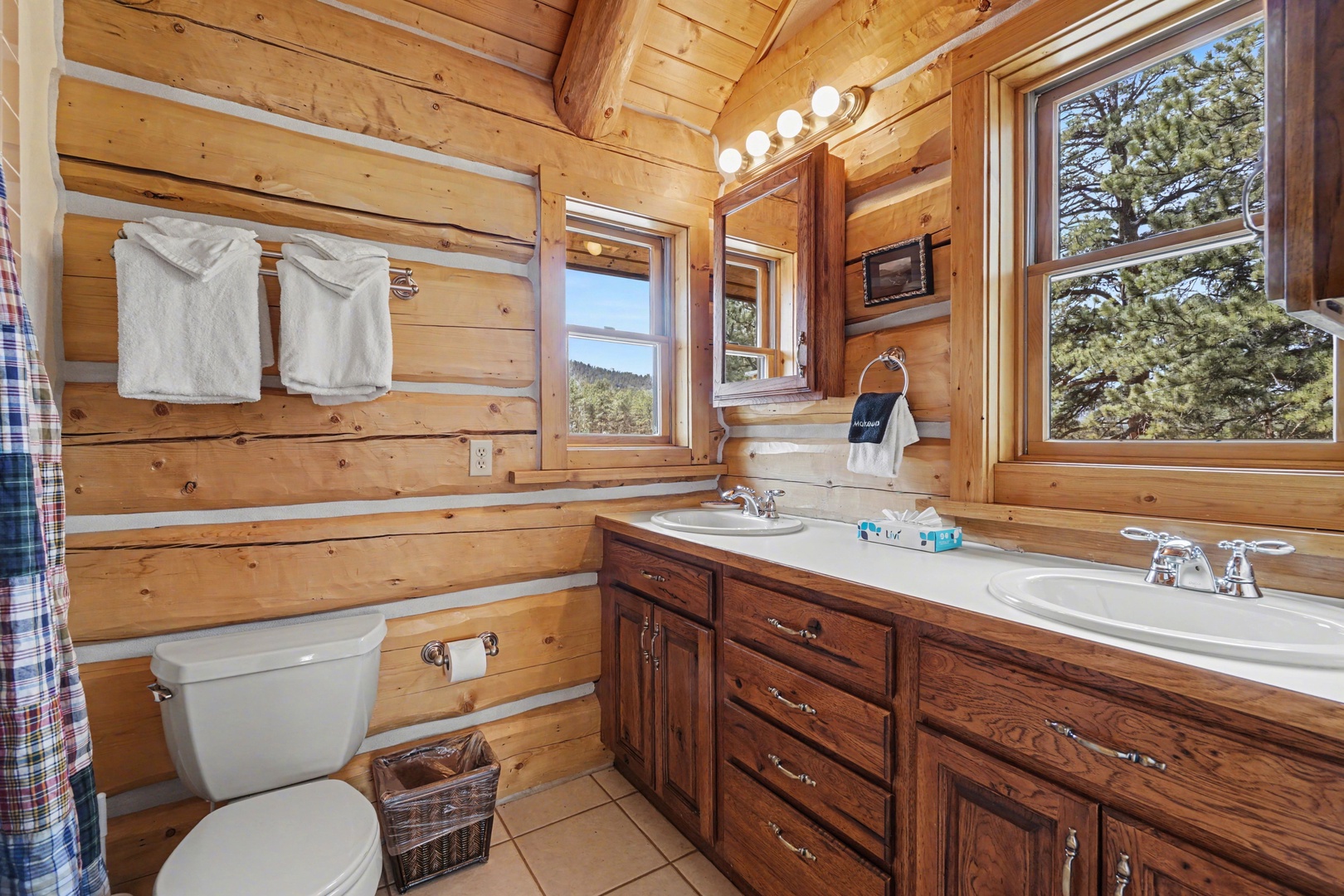 Enjoy the rustic charm of your log cabin bathroom with dual vanity sinks and forest views through the window.