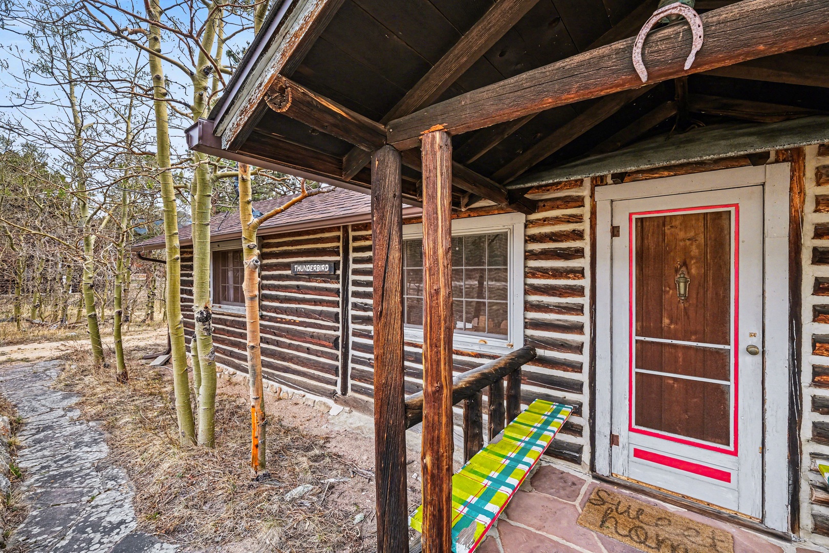 Rustic log cabin exterior featuring covered entry with wooden posts and colorful bench beside the entrance door.