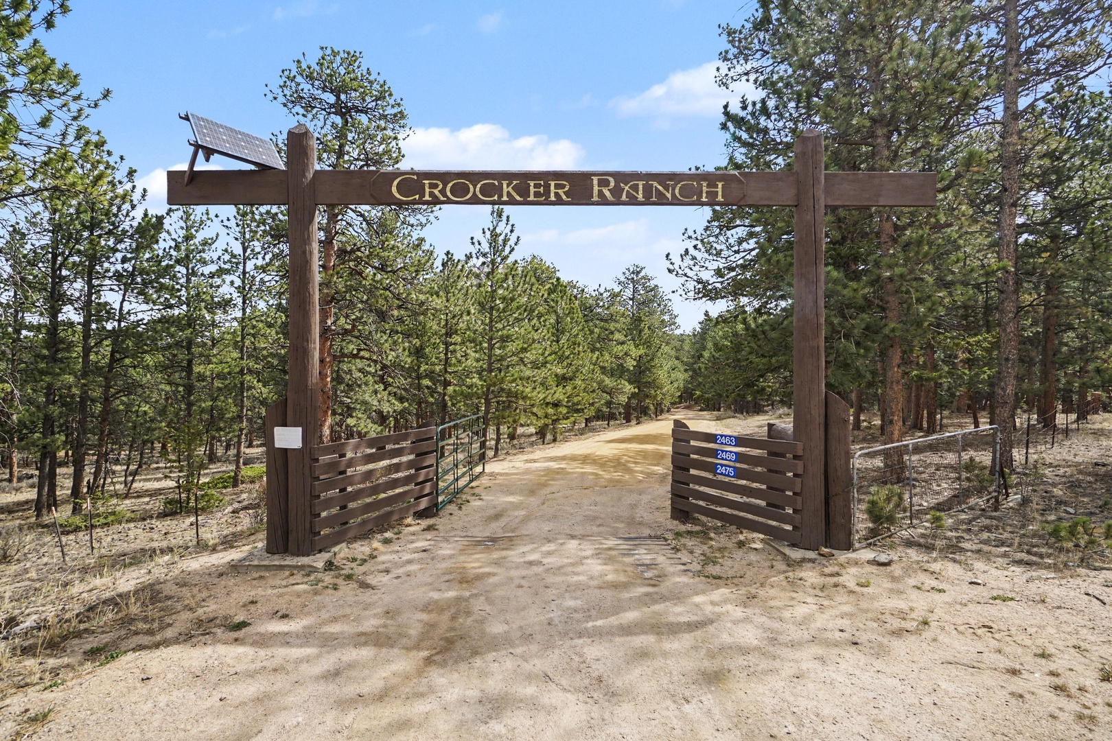 Rustic wooden entrance gate marks the arrival at Crocker Ranch, surrounded by natural pine forest landscape.