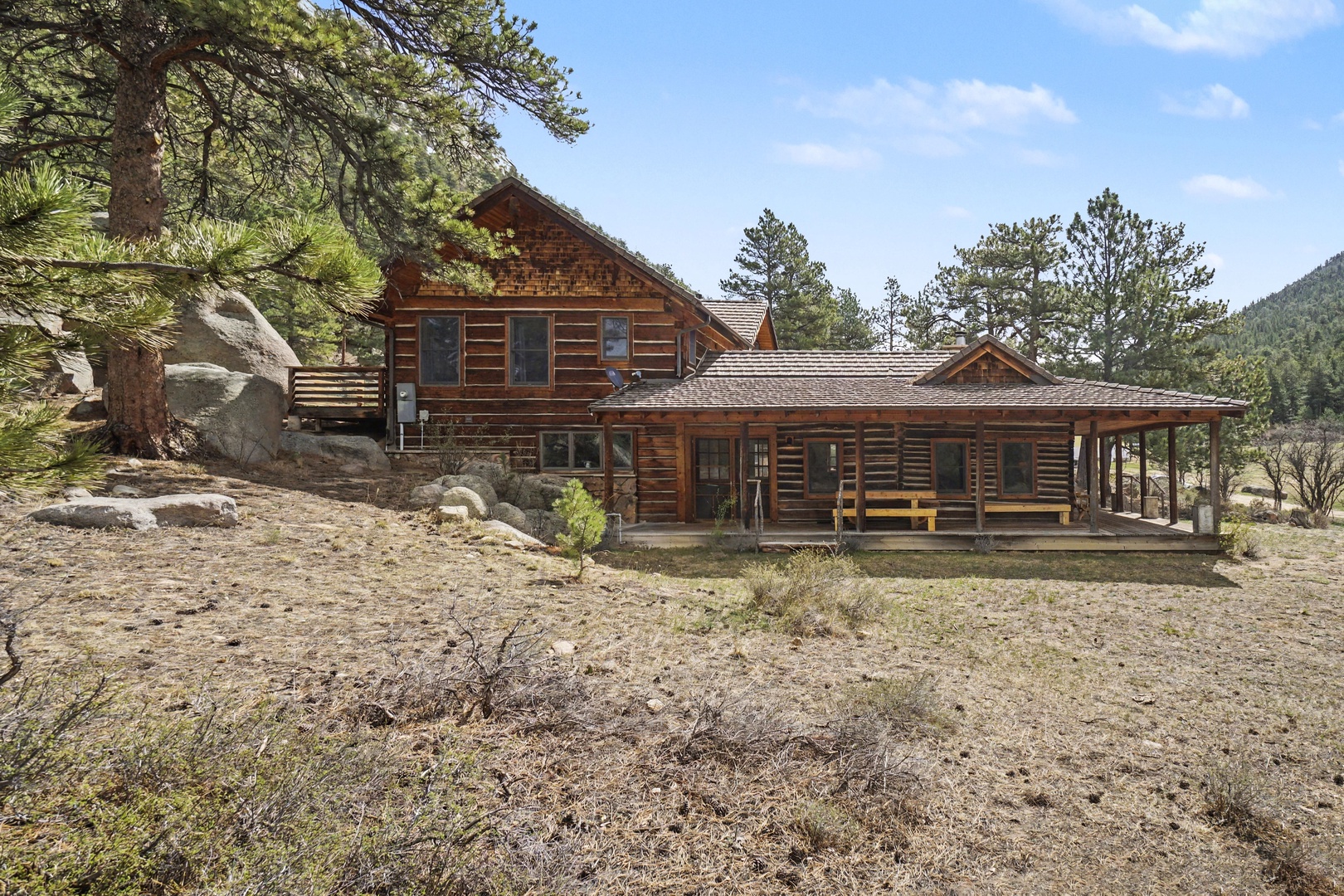 A rustic log cabin retreat nestled among towering pines and granite boulders in a peaceful mountain setting.