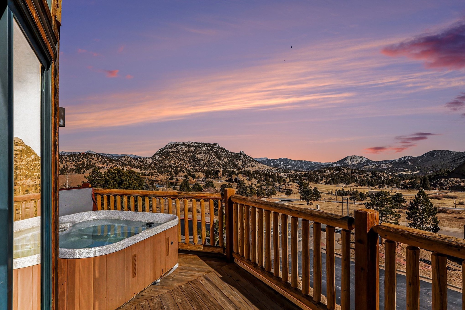 Stunning mountain retreat with private hot tub on deck overlooking dramatic sunrise views across rolling hills and peaks.