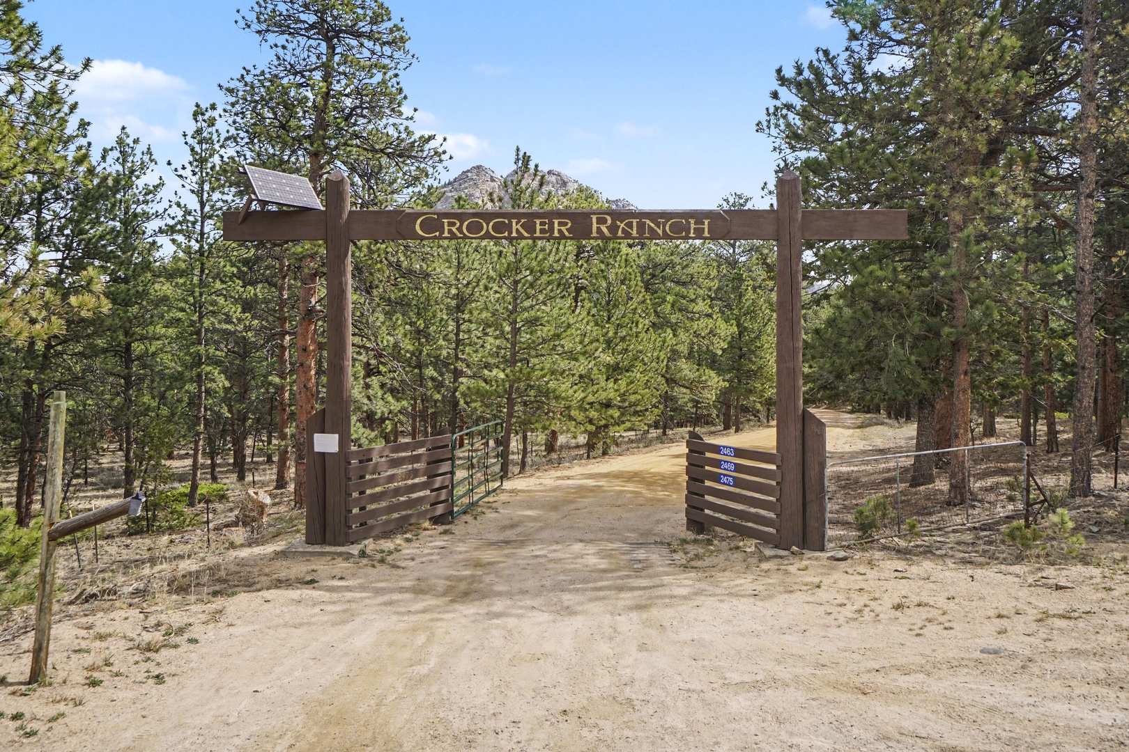 Wooden entrance gate to Crocker Ranch property surrounded by towering pines and mountain views.